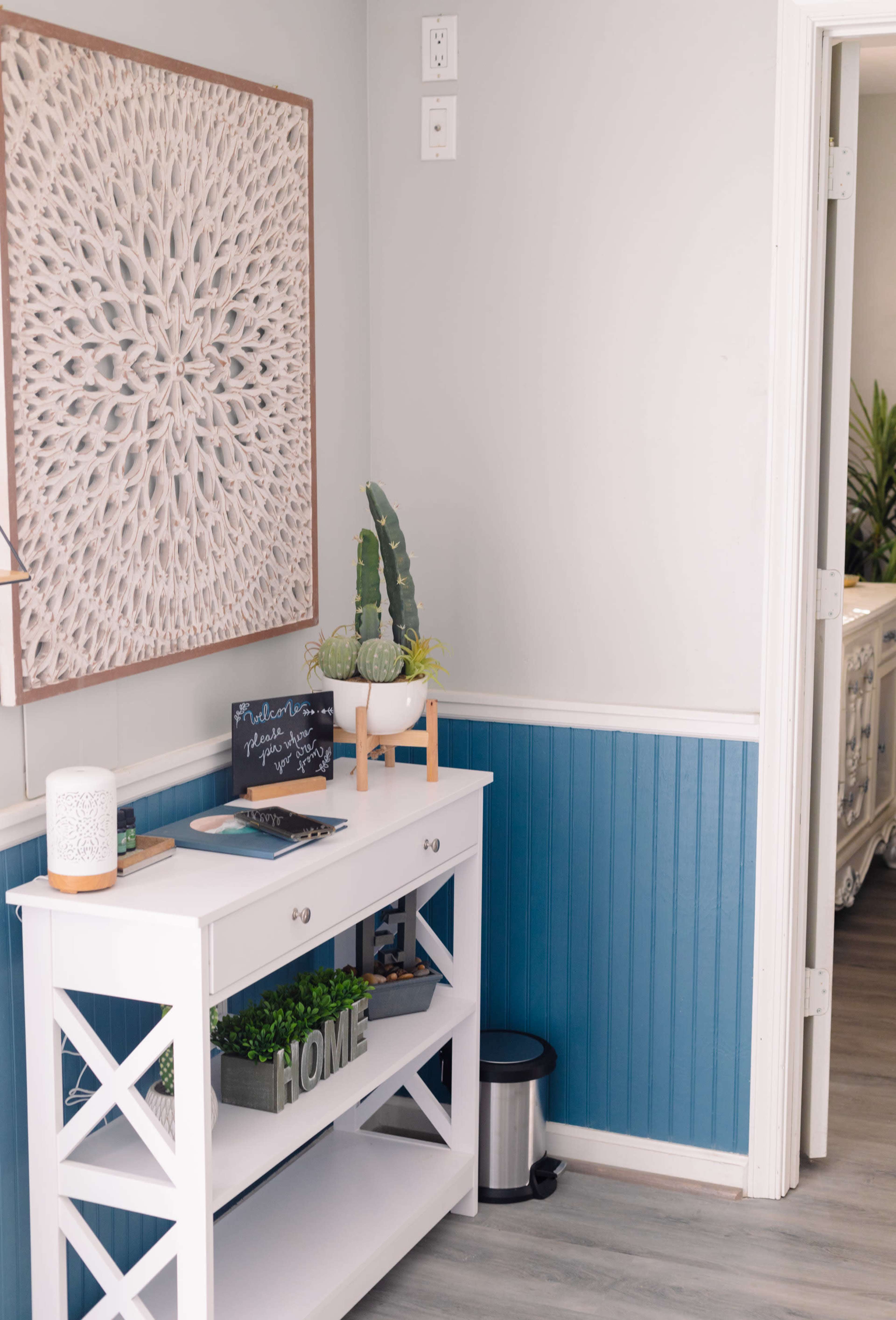 A white console table with decorative items stands against a blue and white wall in a home entryway.