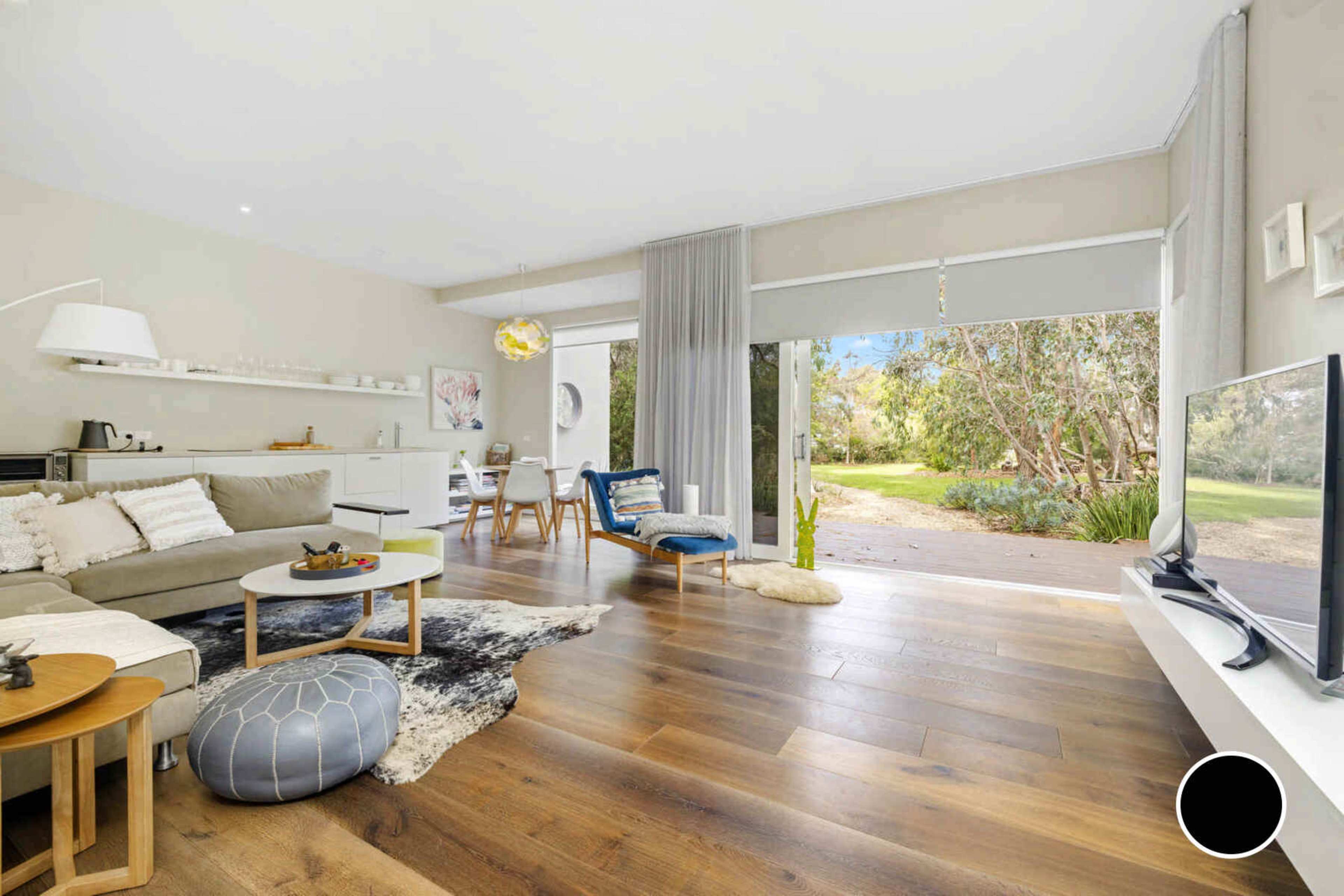 The living room features a light-colored sofa, a round coffee table, and large windows overlooking a garden.