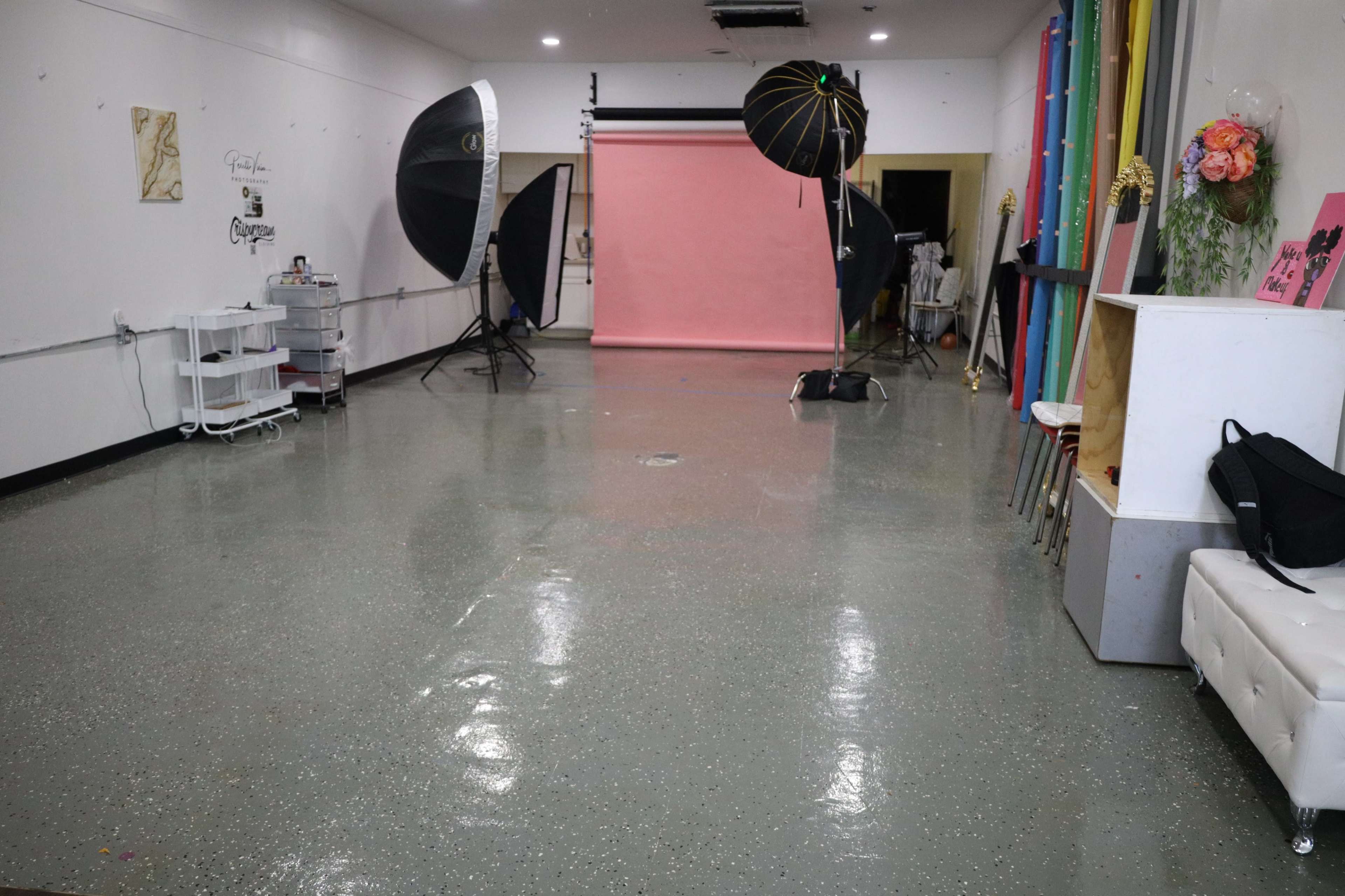 The image shows a photography studio with equipment, including softbox lights and a pink backdrop, set against a polished floor.