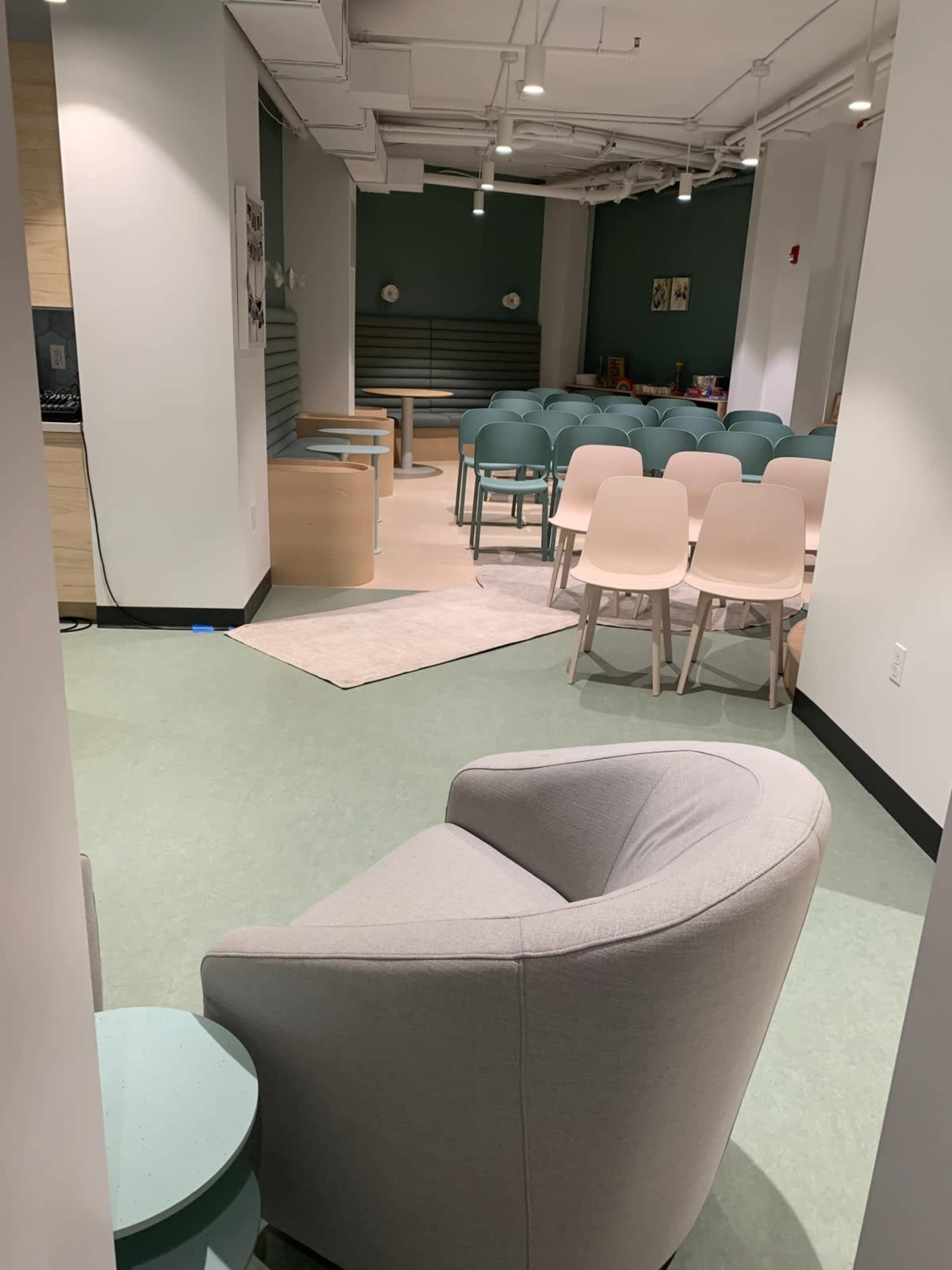 A seating area with a grey armchair and a semi-circle of light-colored chairs arranged for an event in a modern room.