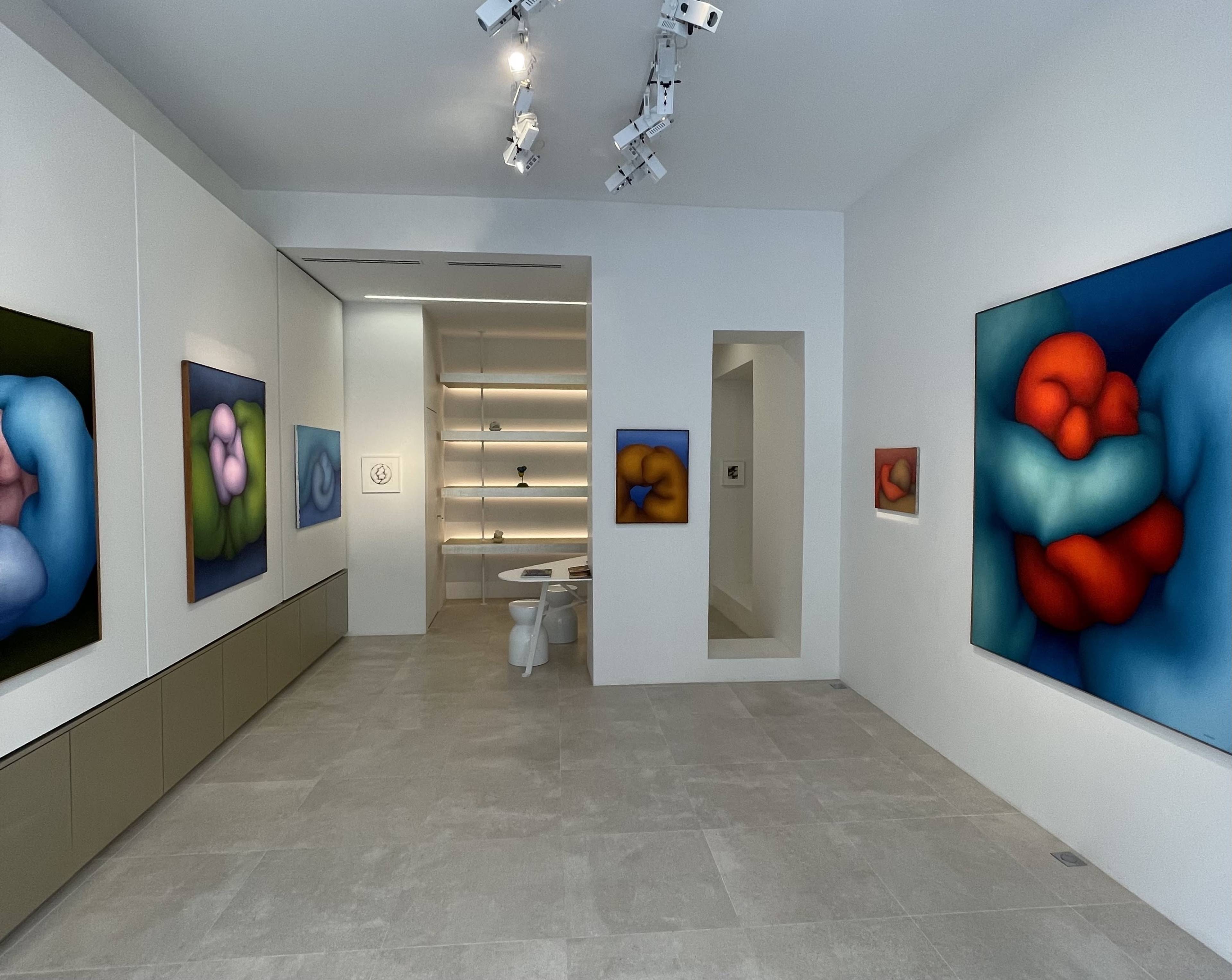 A modern art gallery with abstract paintings on the walls and a minimalist exhibition space featuring a table and a set of stools.