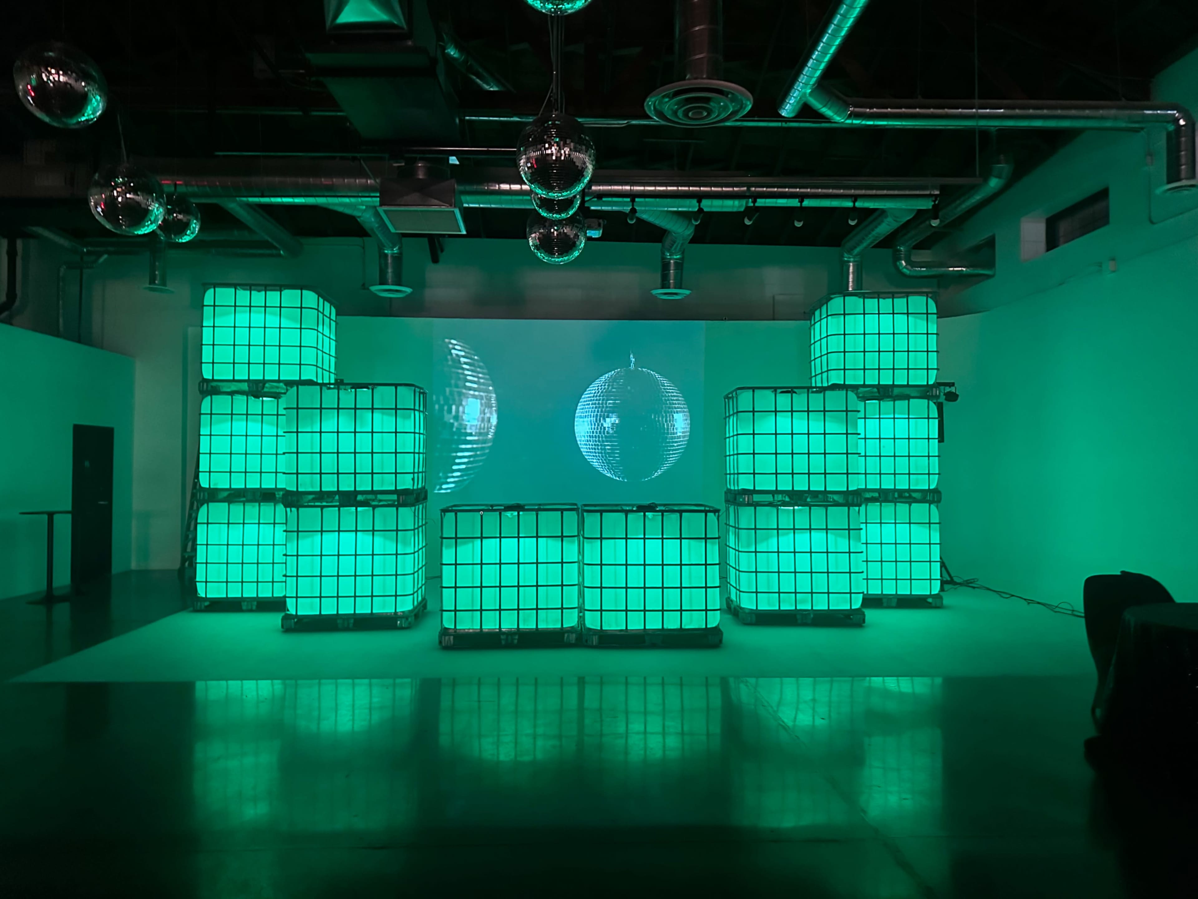 A room features a wall of illuminated green crates with a disco ball and projected visuals in the background.