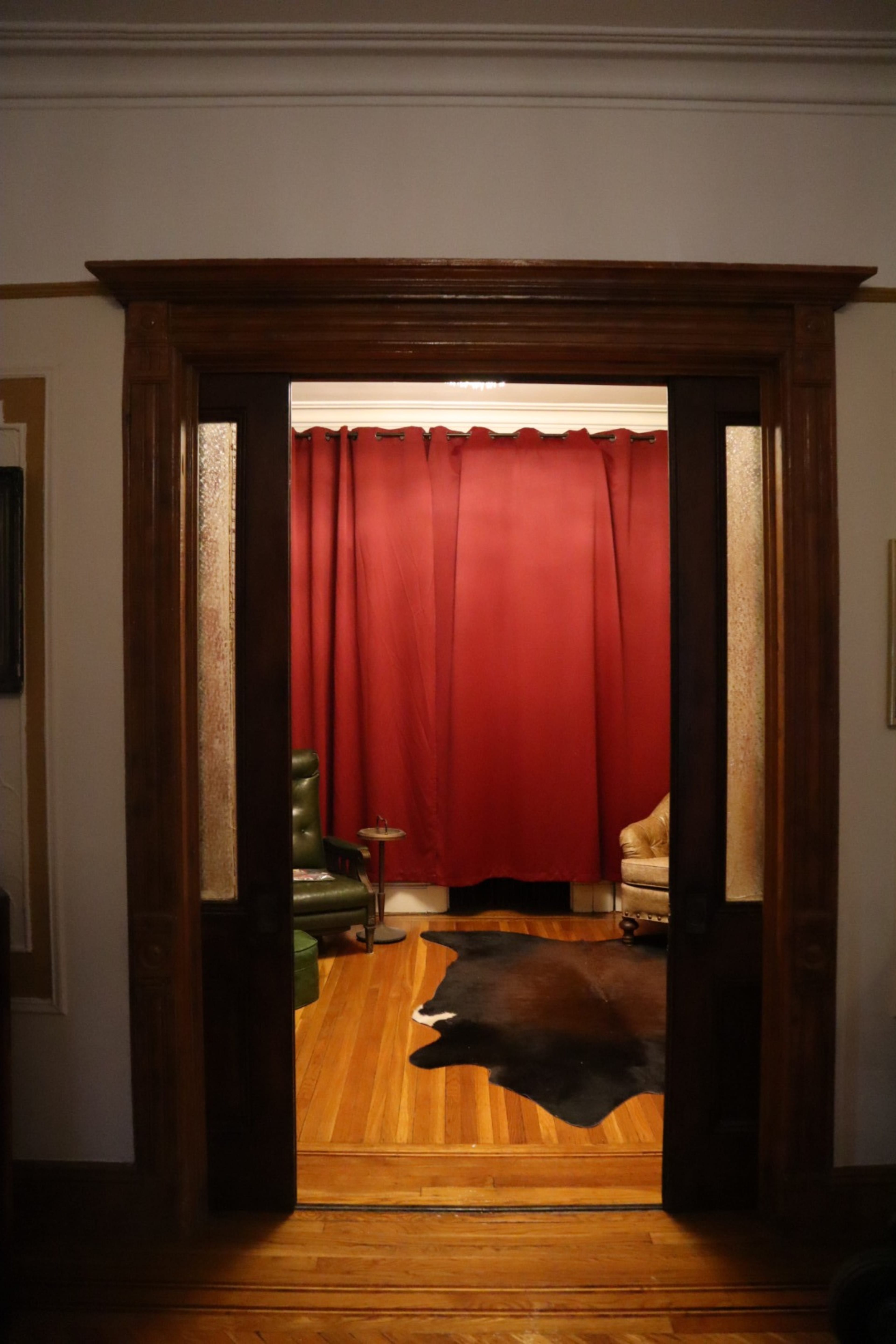 A doorway leads into a room with wooden floors, a red curtain in the background, and a cowhide rug on the floor.