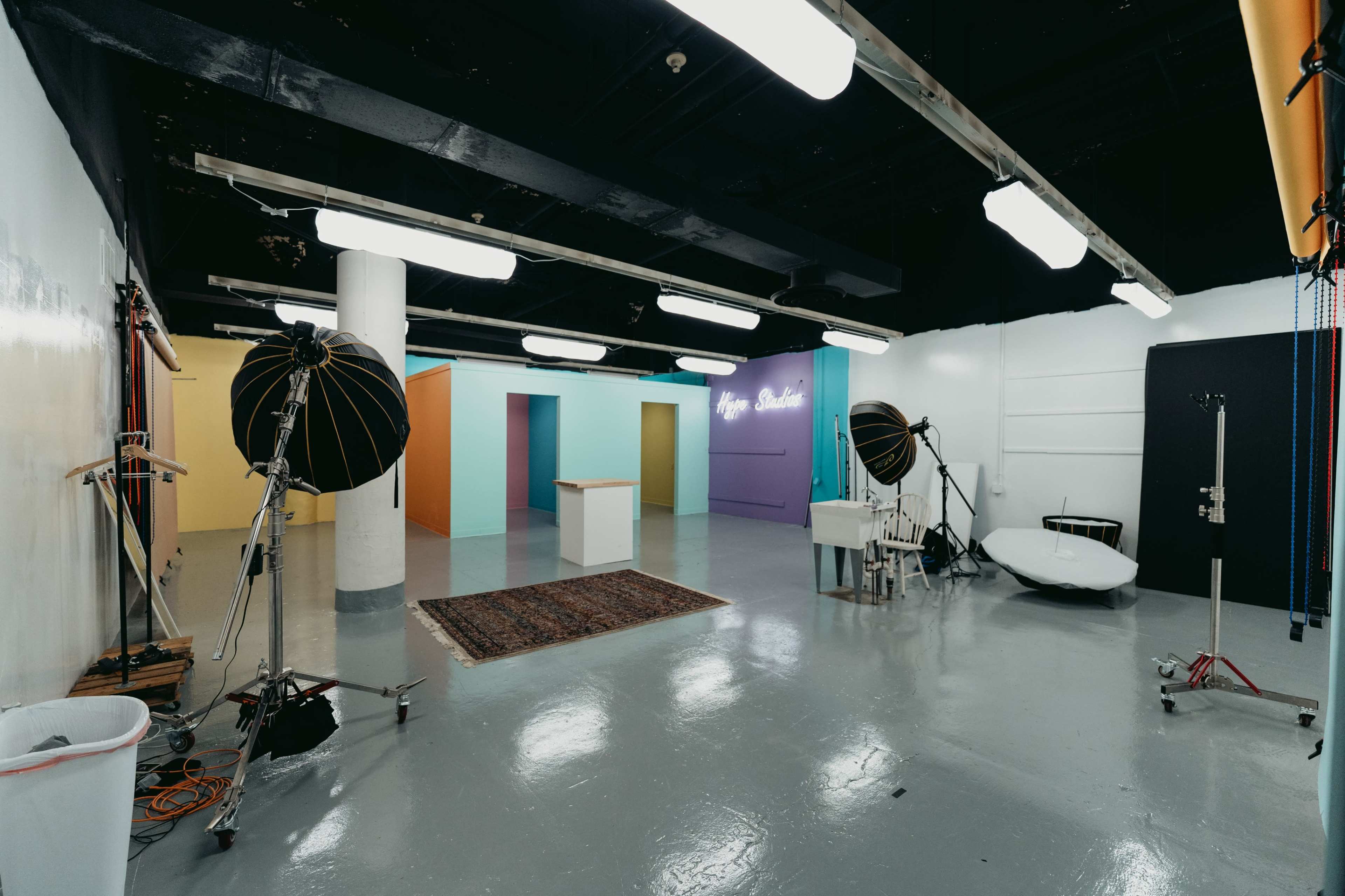 A spacious photo studio with bright colored walls, a white backdrop, lighting equipment, and various props arranged throughout the room.