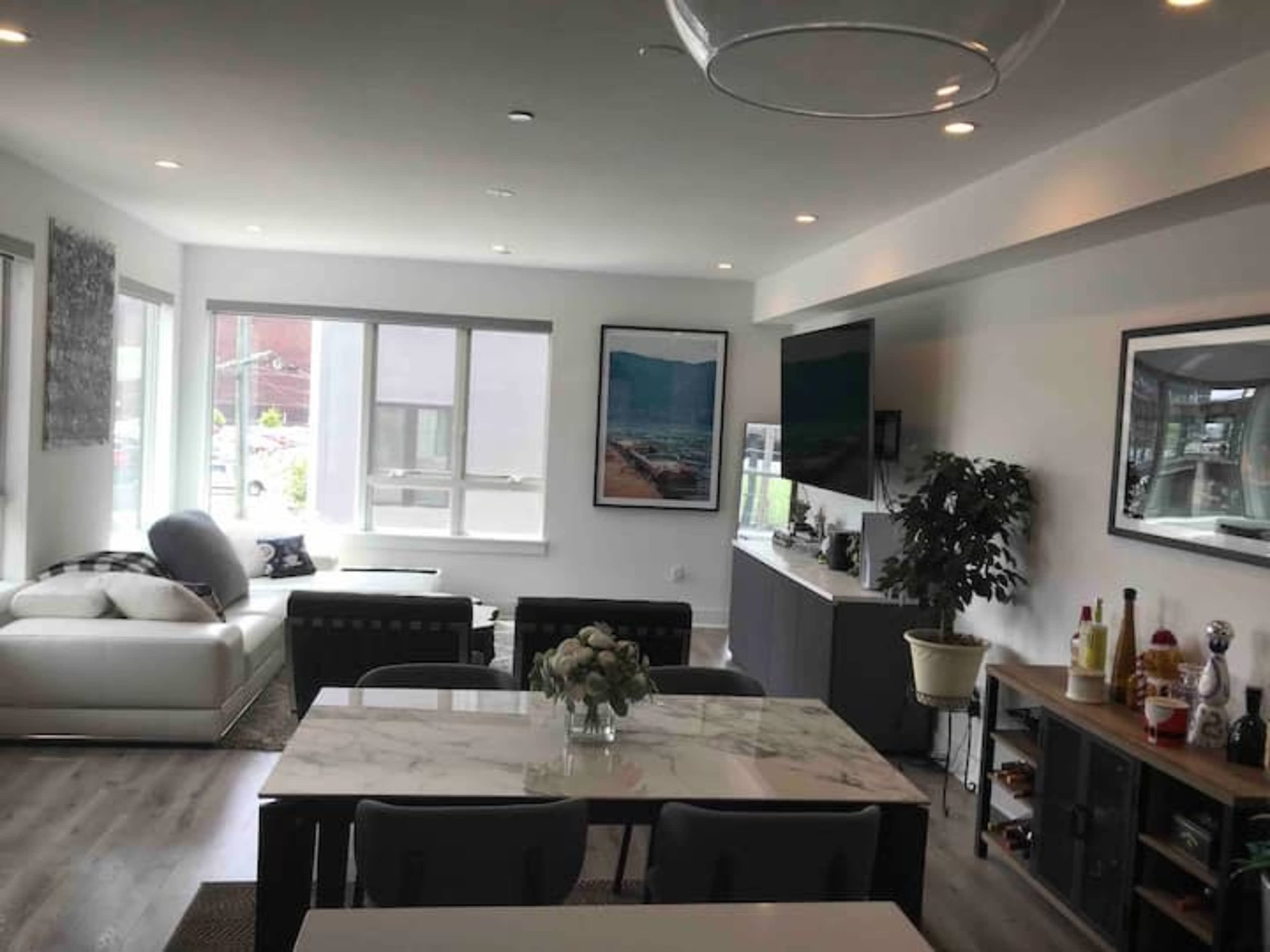 A modern living and dining area featuring a sectional sofa, a dining table with chairs, and a media console with a television.