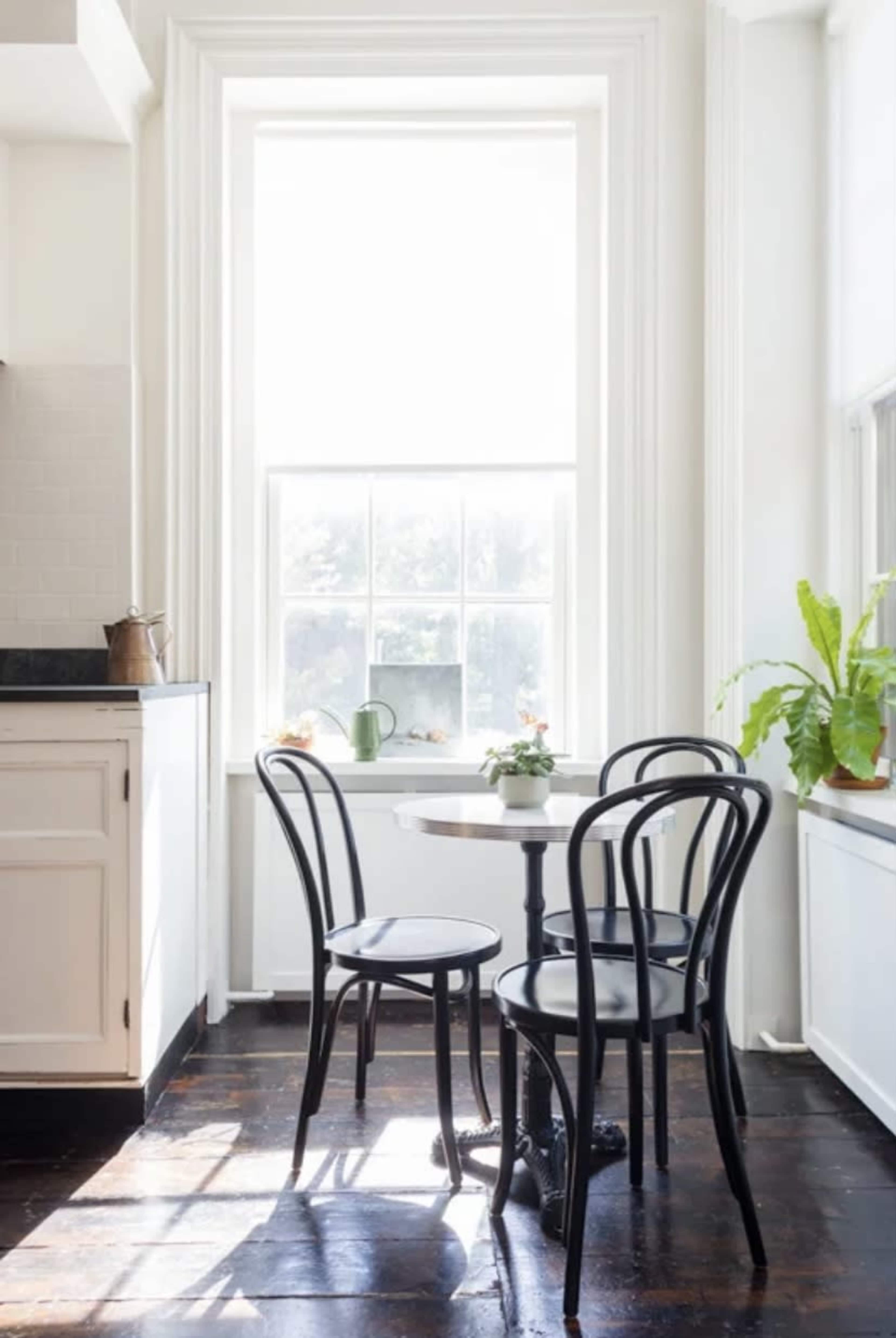 A small round table with four black chairs sits near a large window in a bright kitchen.