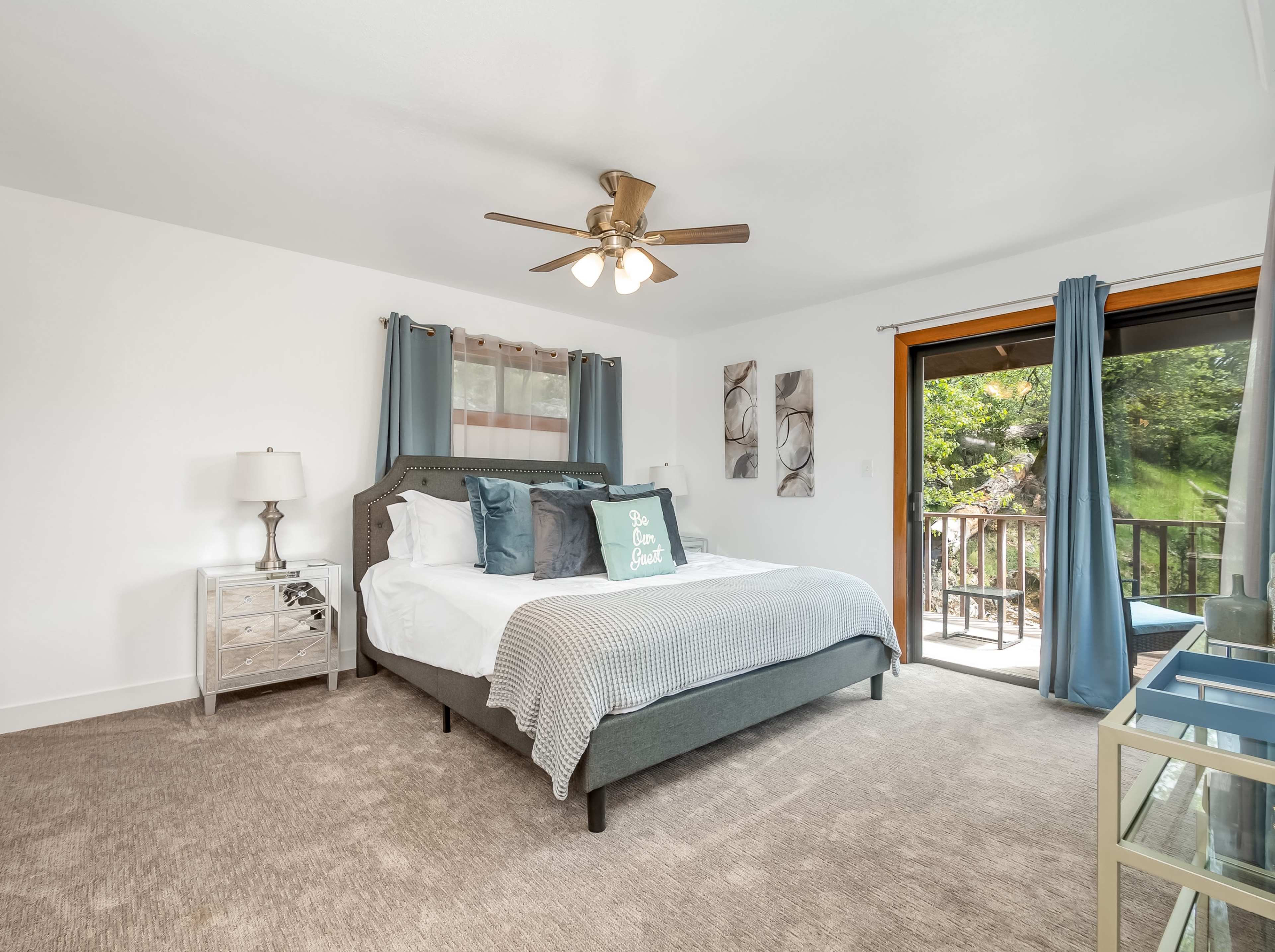A neatly arranged bedroom with a large bed, two bedside lamps, and a sliding door leading to a balcony with a view of greenery.