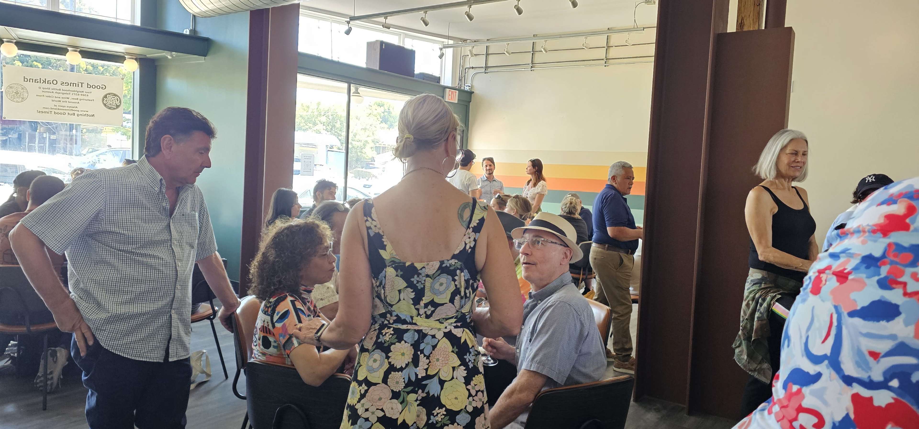 A group of people is gathered inside a cafe, engaged in conversation while others stand nearby.