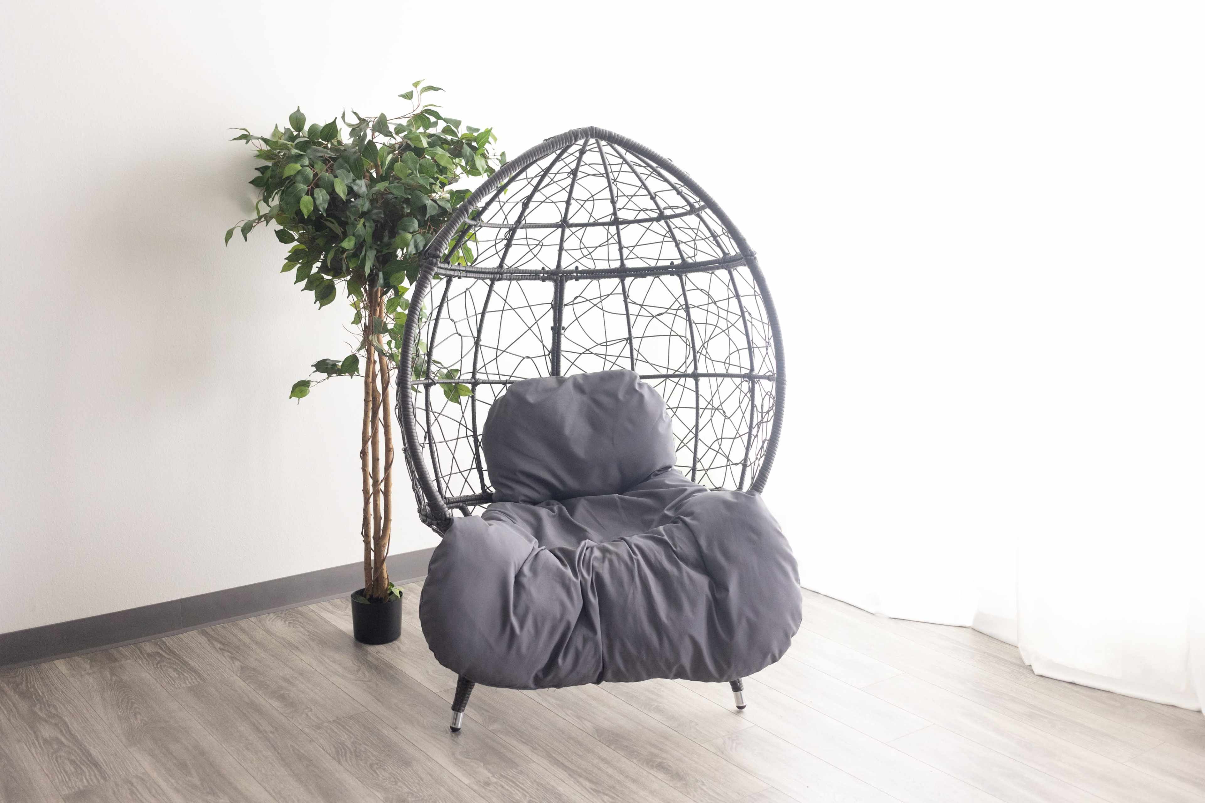 A large, cushioned, egg-shaped chair stands beside a potted tree in a brightly lit room.