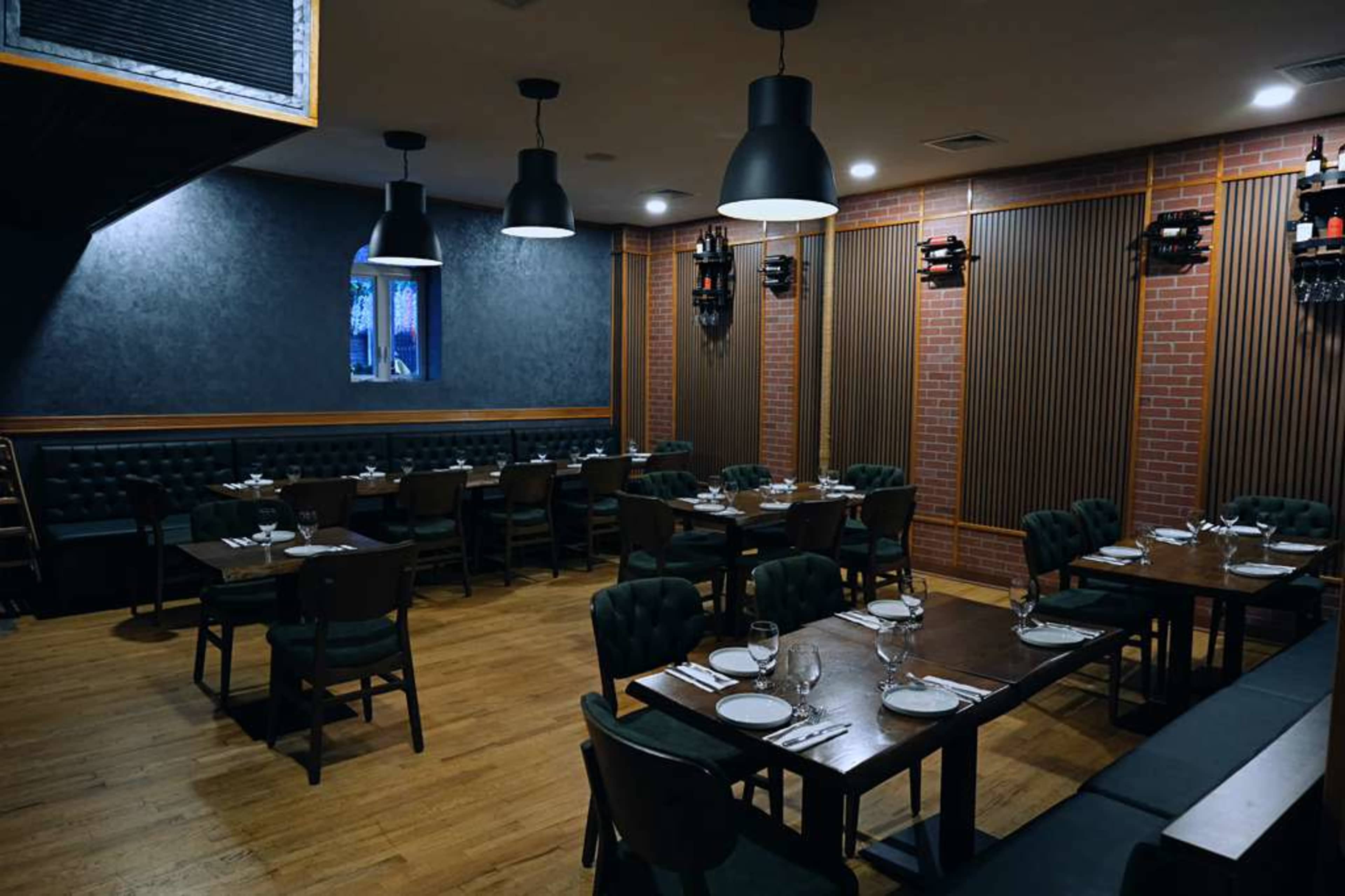 The image shows an interior of a modern restaurant with wooden floors, dark walls, and neatly arranged tables set for dining.