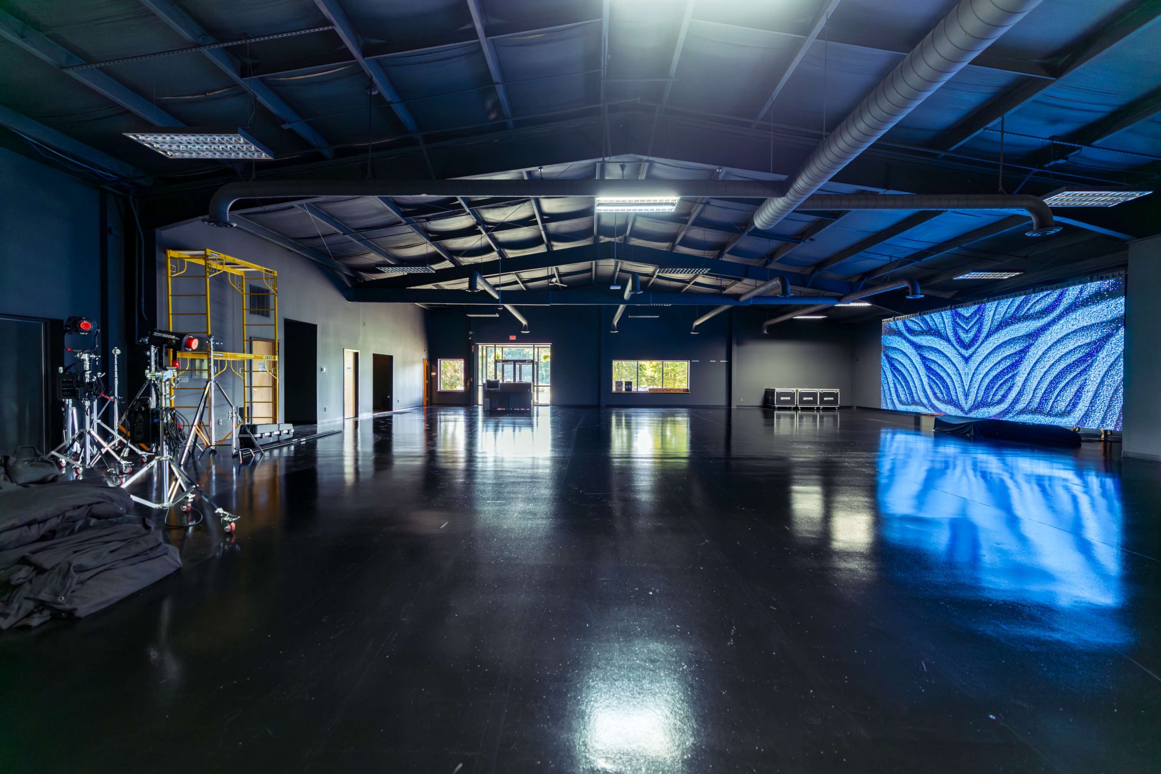 The image shows a spacious, modern interior with a polished black floor, large windows, and a vibrant digital display on one wall.