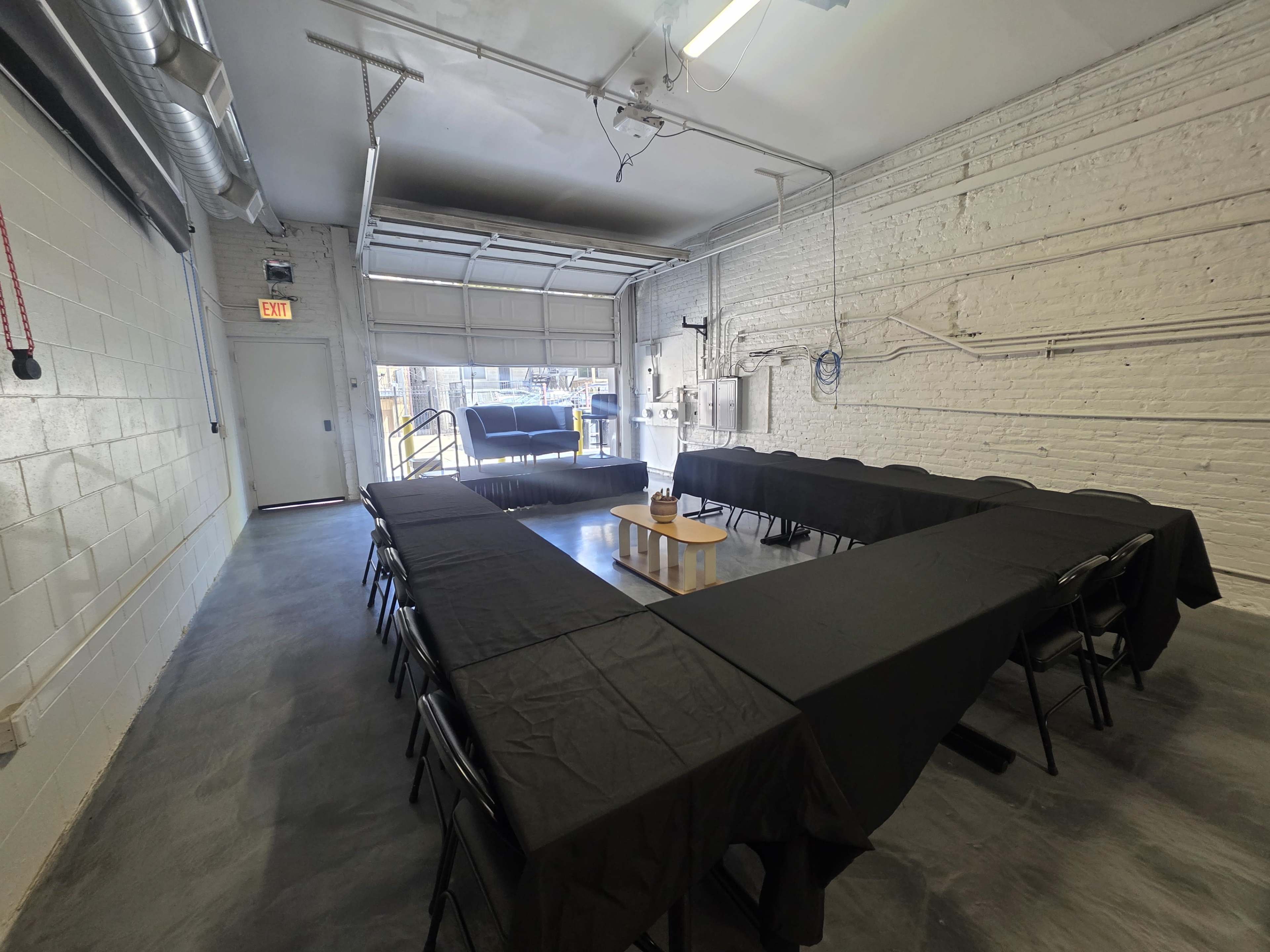The image shows a spacious meeting room with a large, rectangular table arrangement covered in black tablecloths and chairs aligned around it.