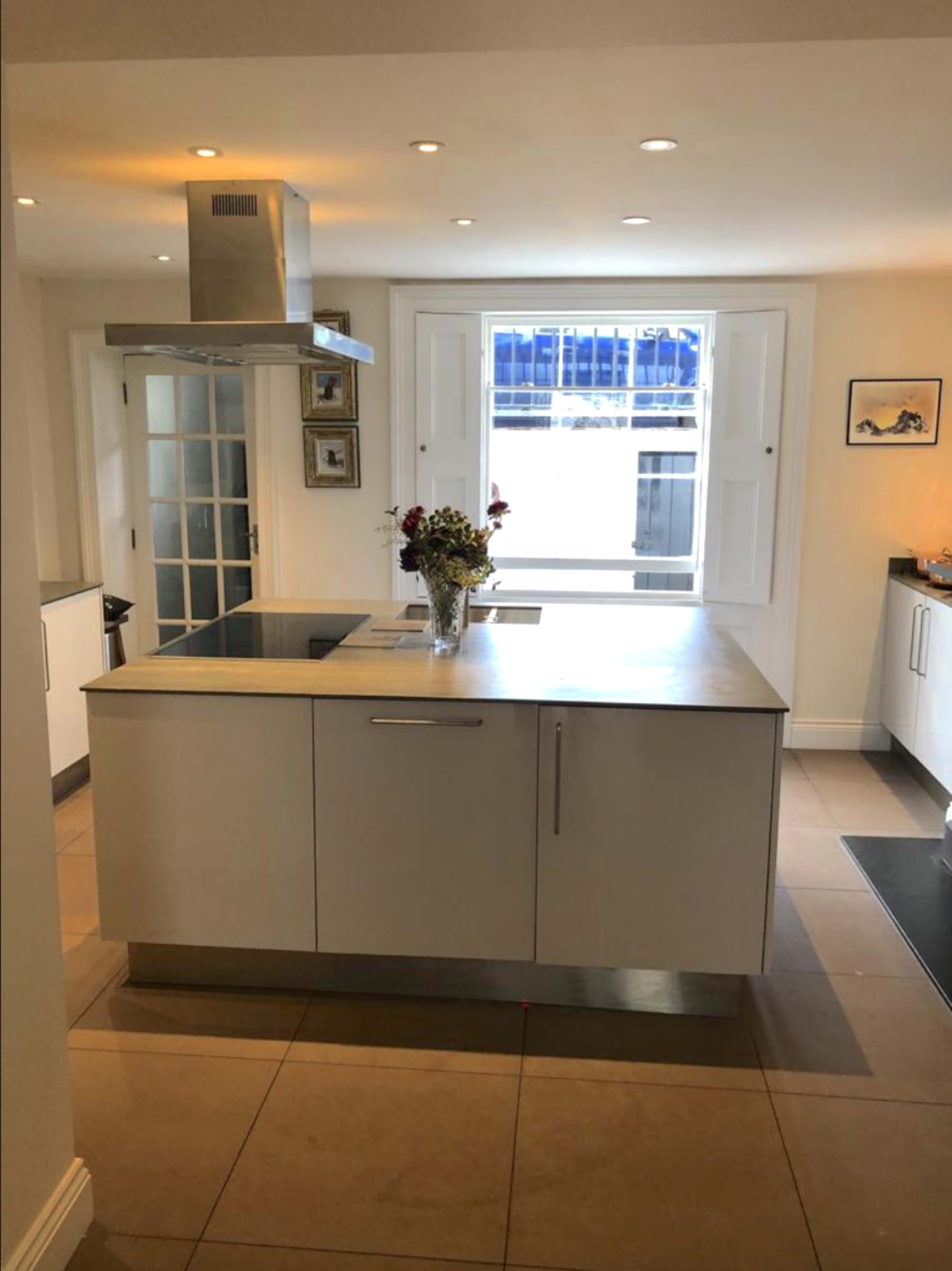 A modern kitchen with a central island, a window above the sink, and white cabinetry.