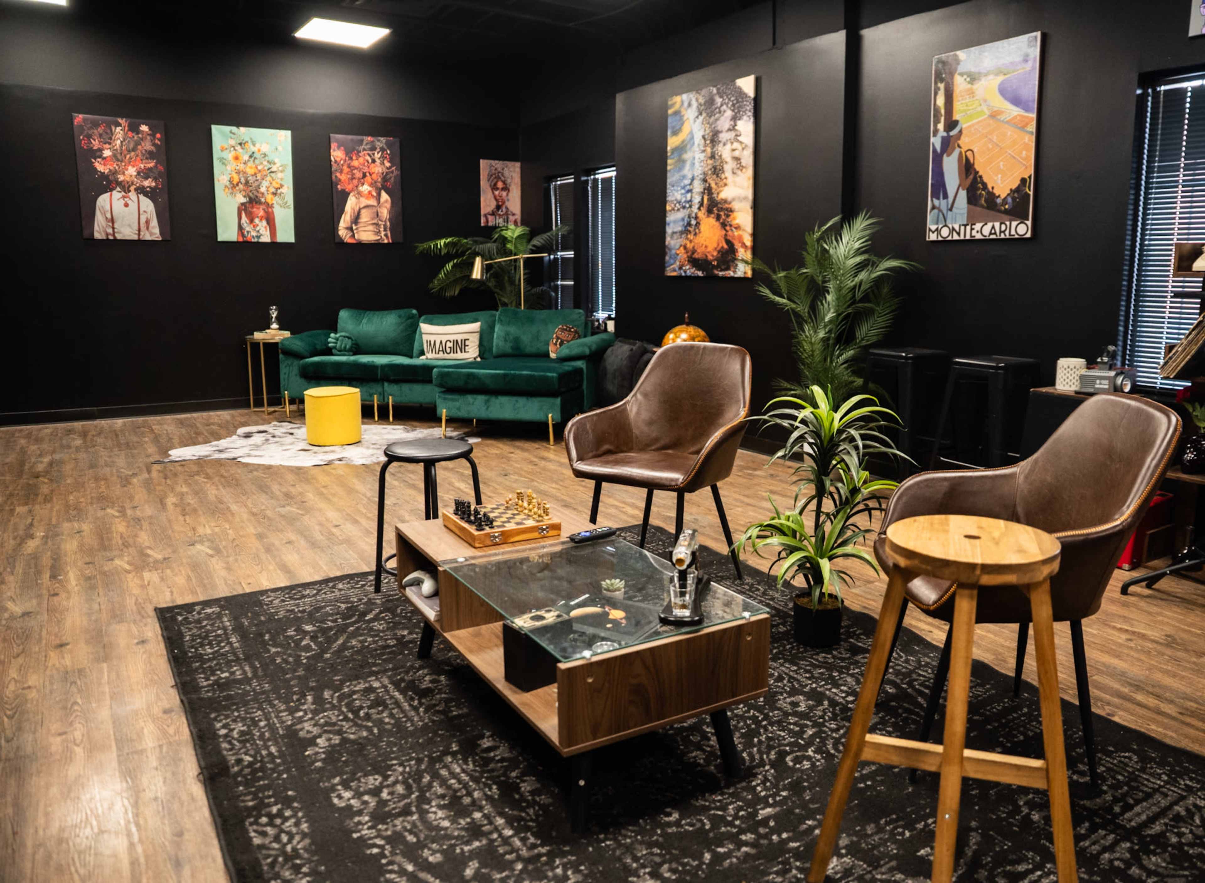 The image depicts a modern lounge area with a green sofa, two chairs, a coffee table, and artwork on black walls.