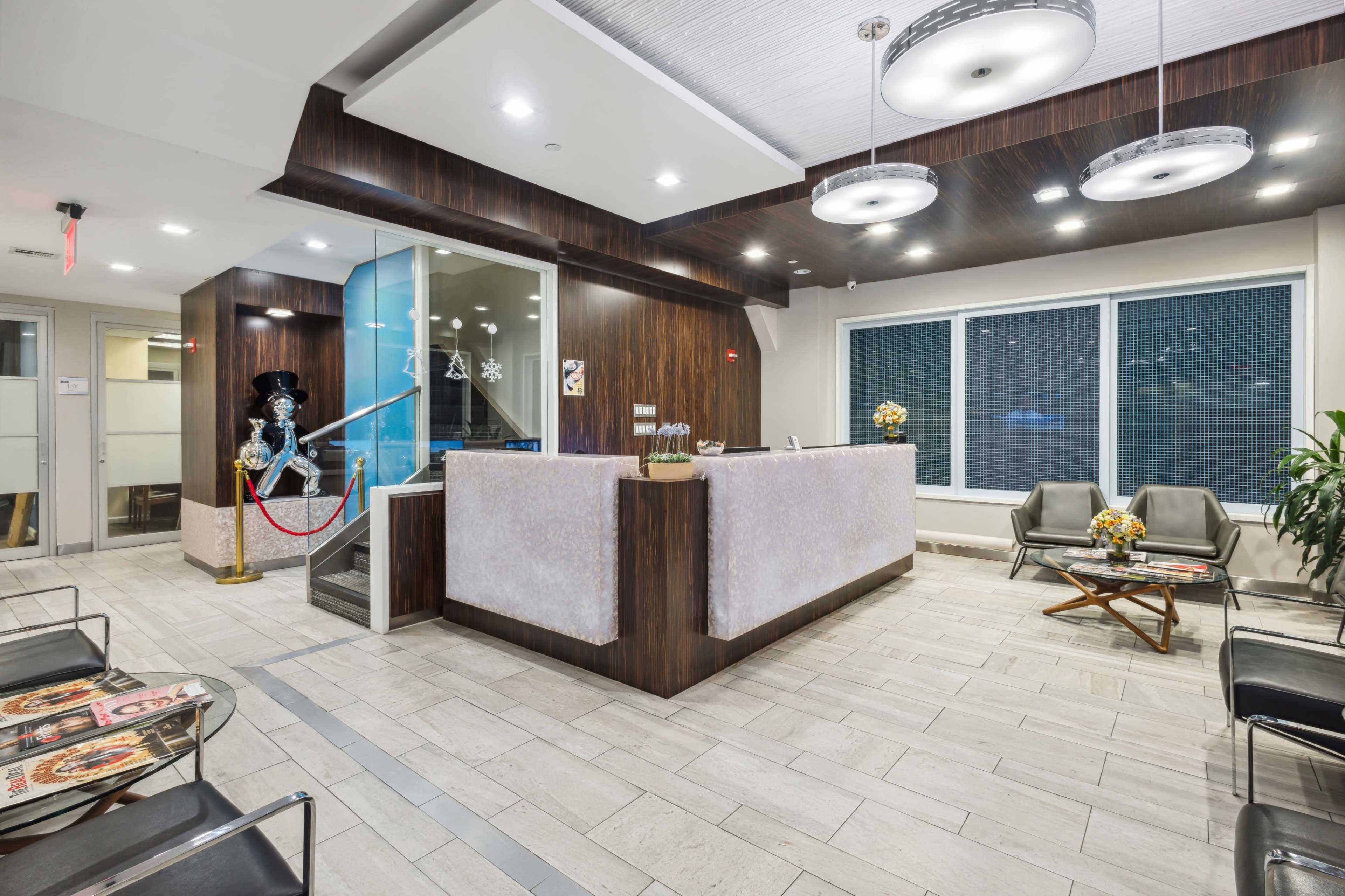 A modern reception area with a front desk, seating, large windows, and decorative elements, including a mannequin and floral arrangements.