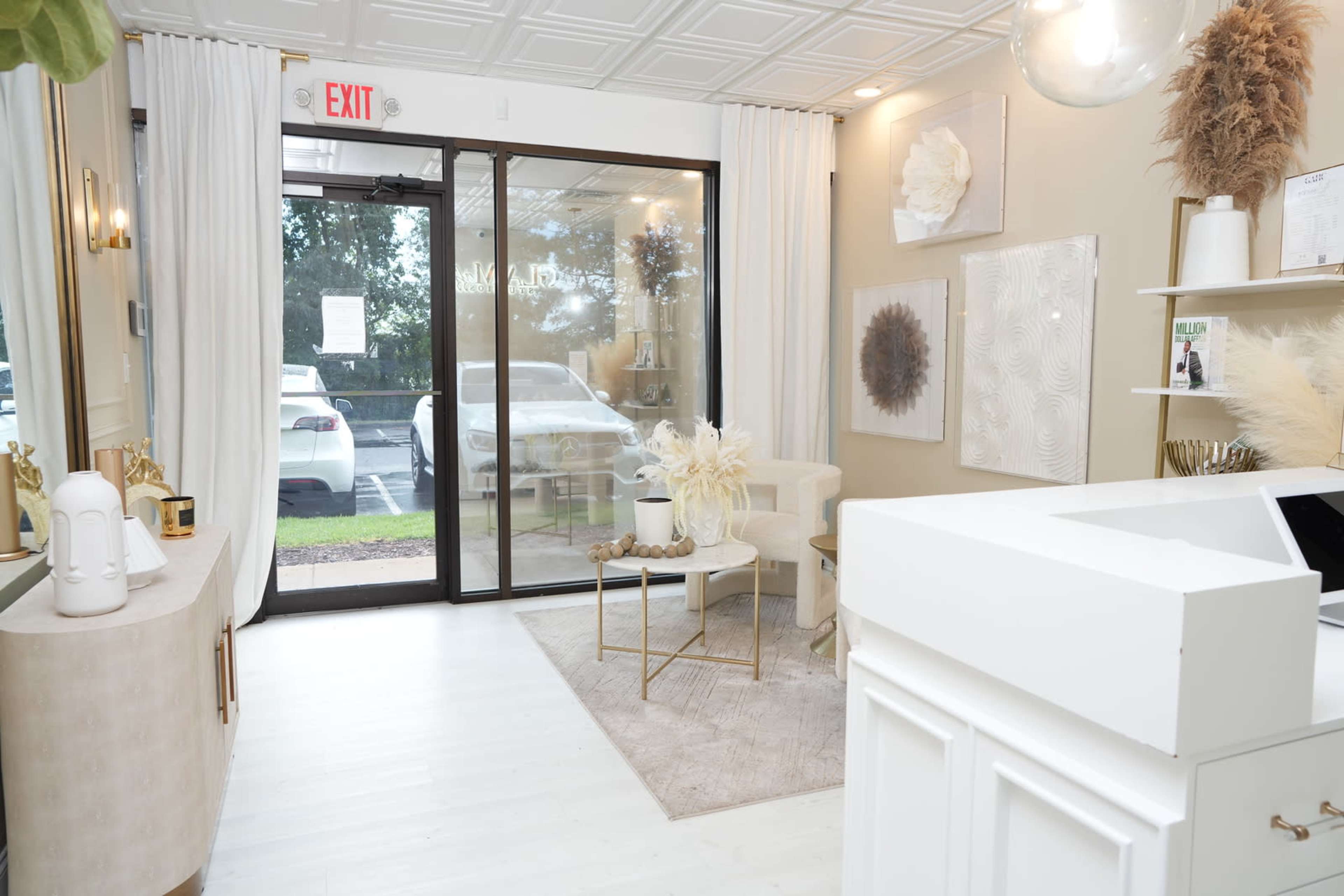 A modern reception area with neutral decor, featuring a small seating arrangement, decorative wall art, and a large glass entrance.