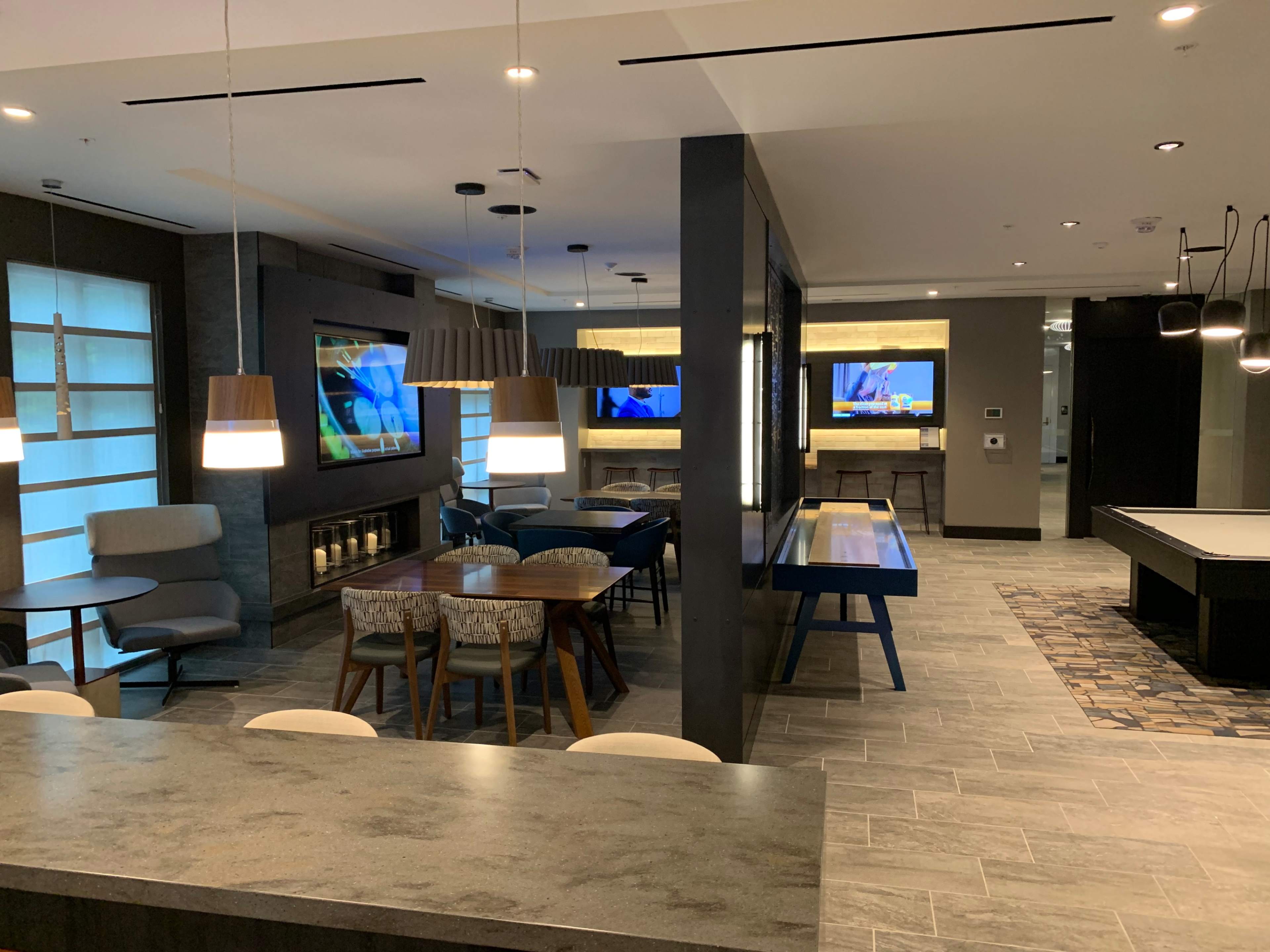 A modern communal space with couches, tables, and large televisions mounted on the walls.