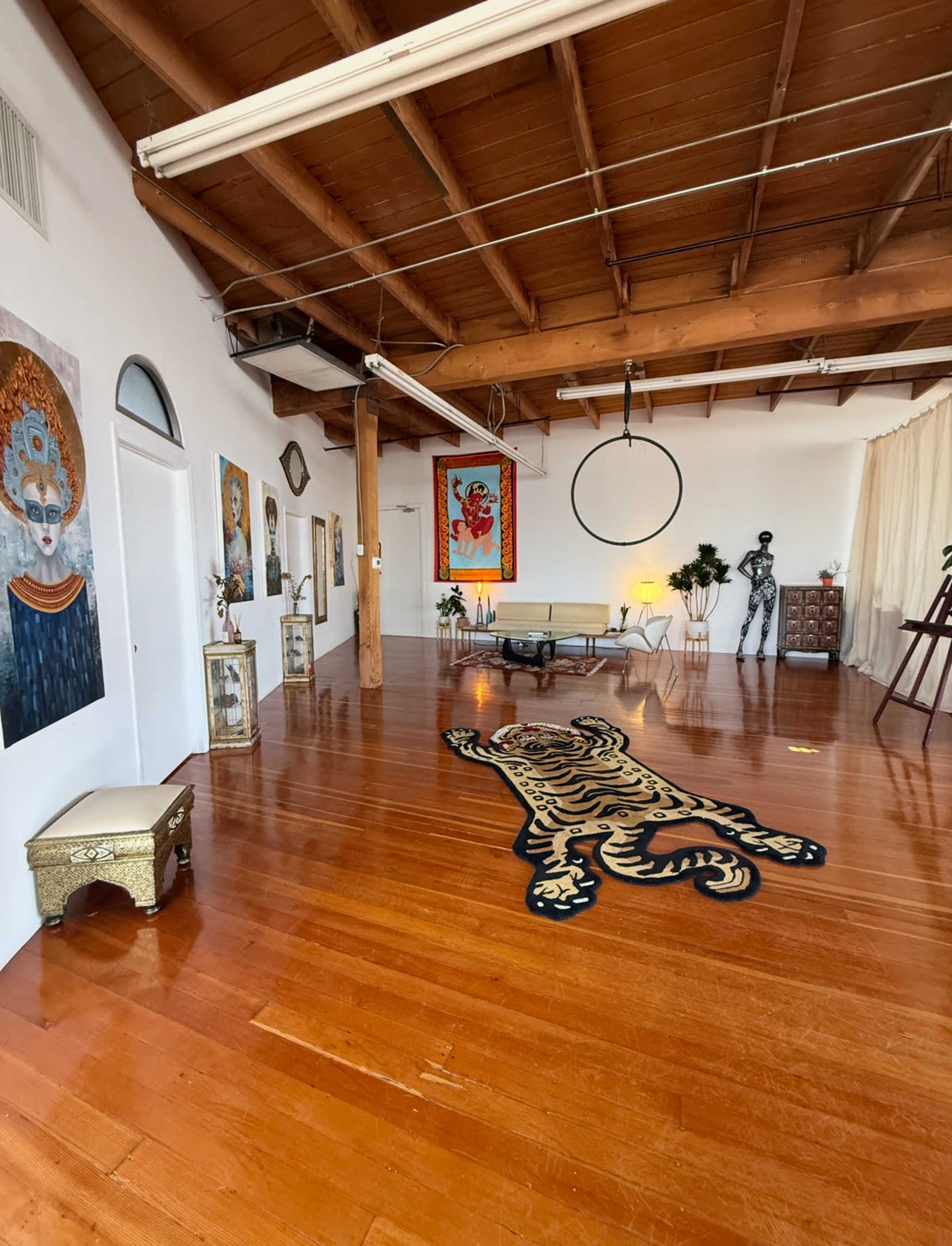 The spacious room has wooden flooring and walls adorned with various artworks, including a large tiger rug and a distinct seating area.