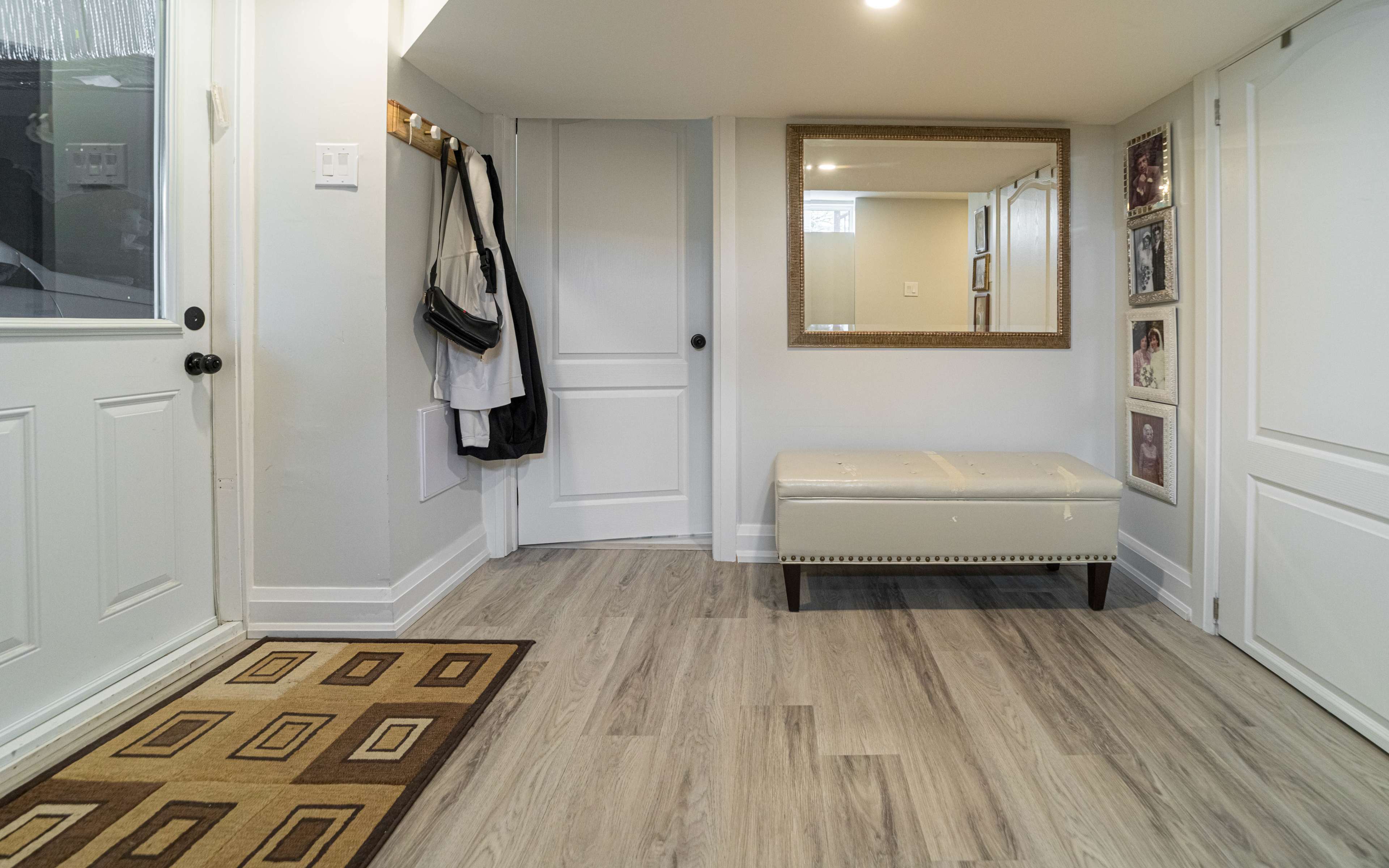 A foyer with a bench, a mirror on the wall, a coat rack, and a door leading outside.