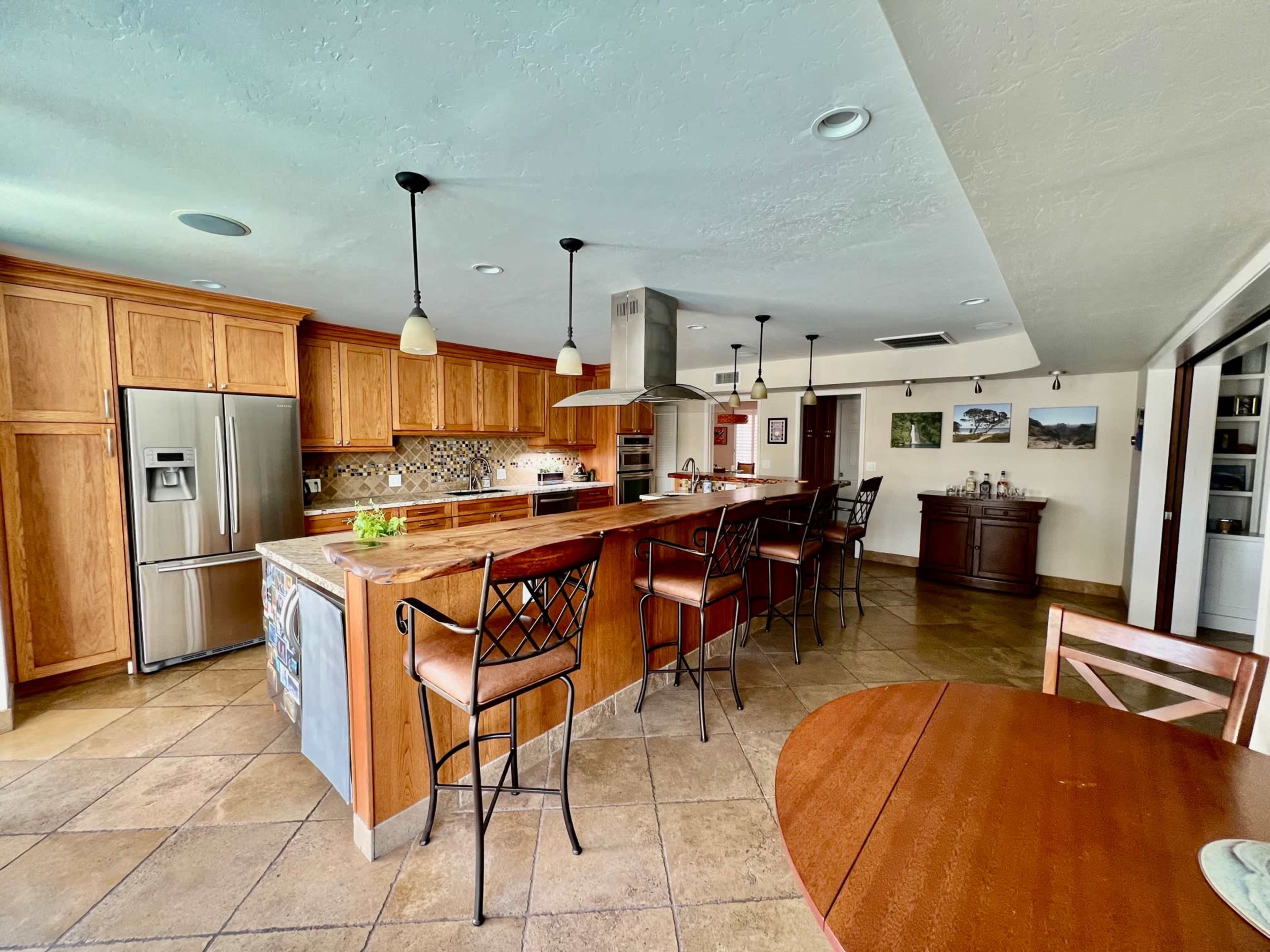 The kitchen features wooden cabinetry, a large island with bar seating, stainless steel appliances, and a dining area with a round table.
