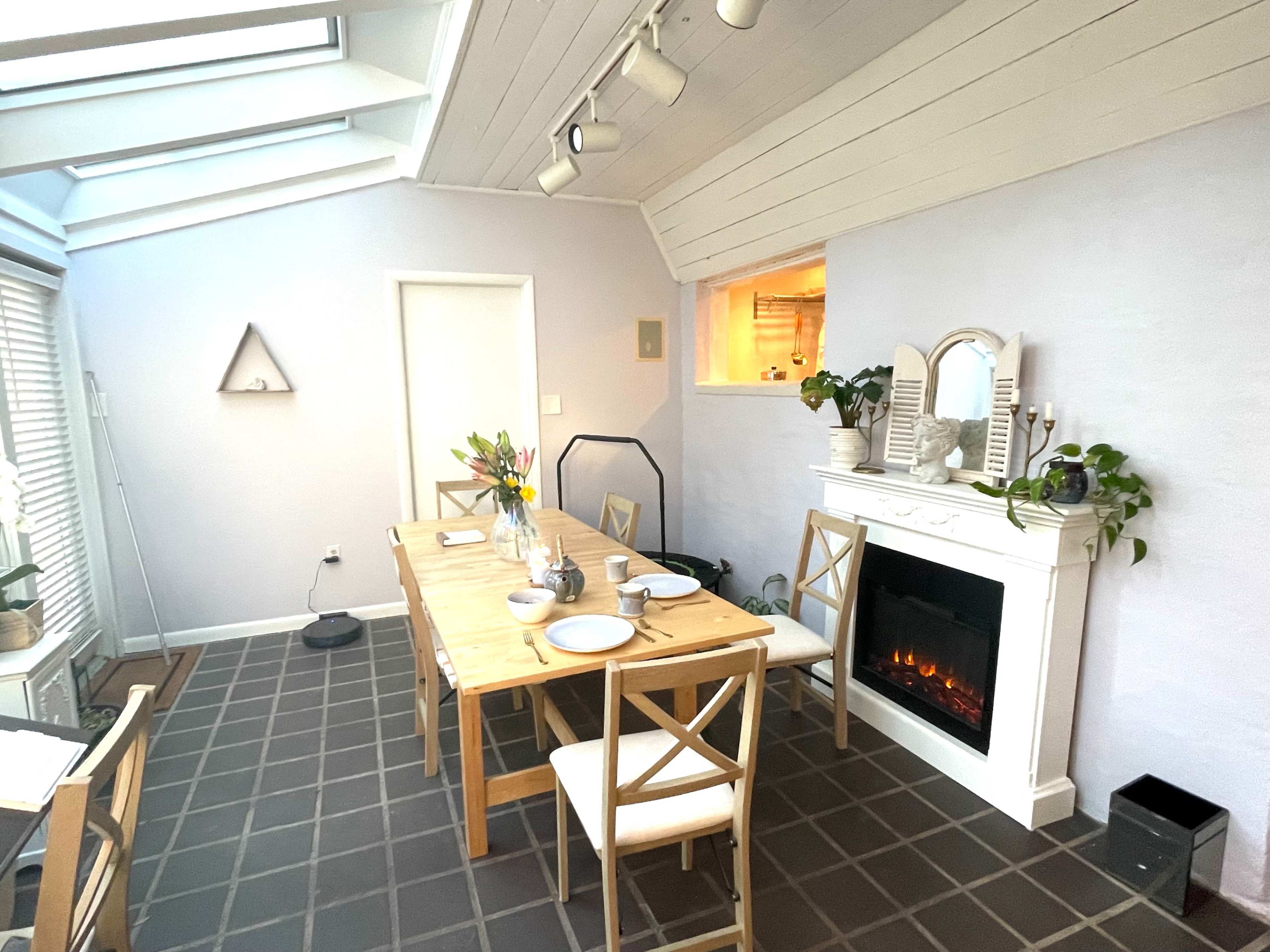 A dining area with a wooden table set for a meal, a modern fireplace, and a large skylight above.