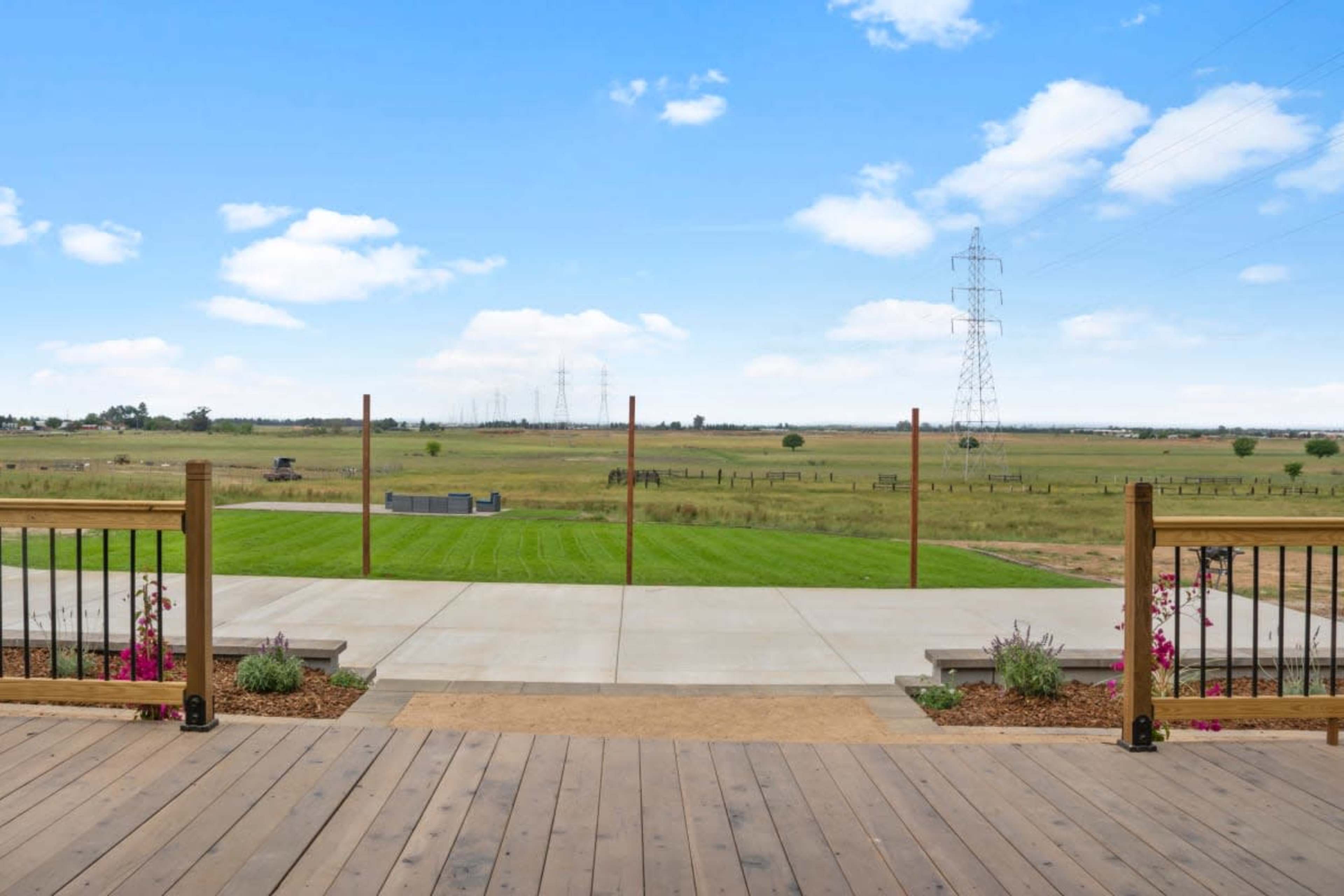 The image shows a wooden deck overlooking a grassy field with power lines and distant structures in the background.