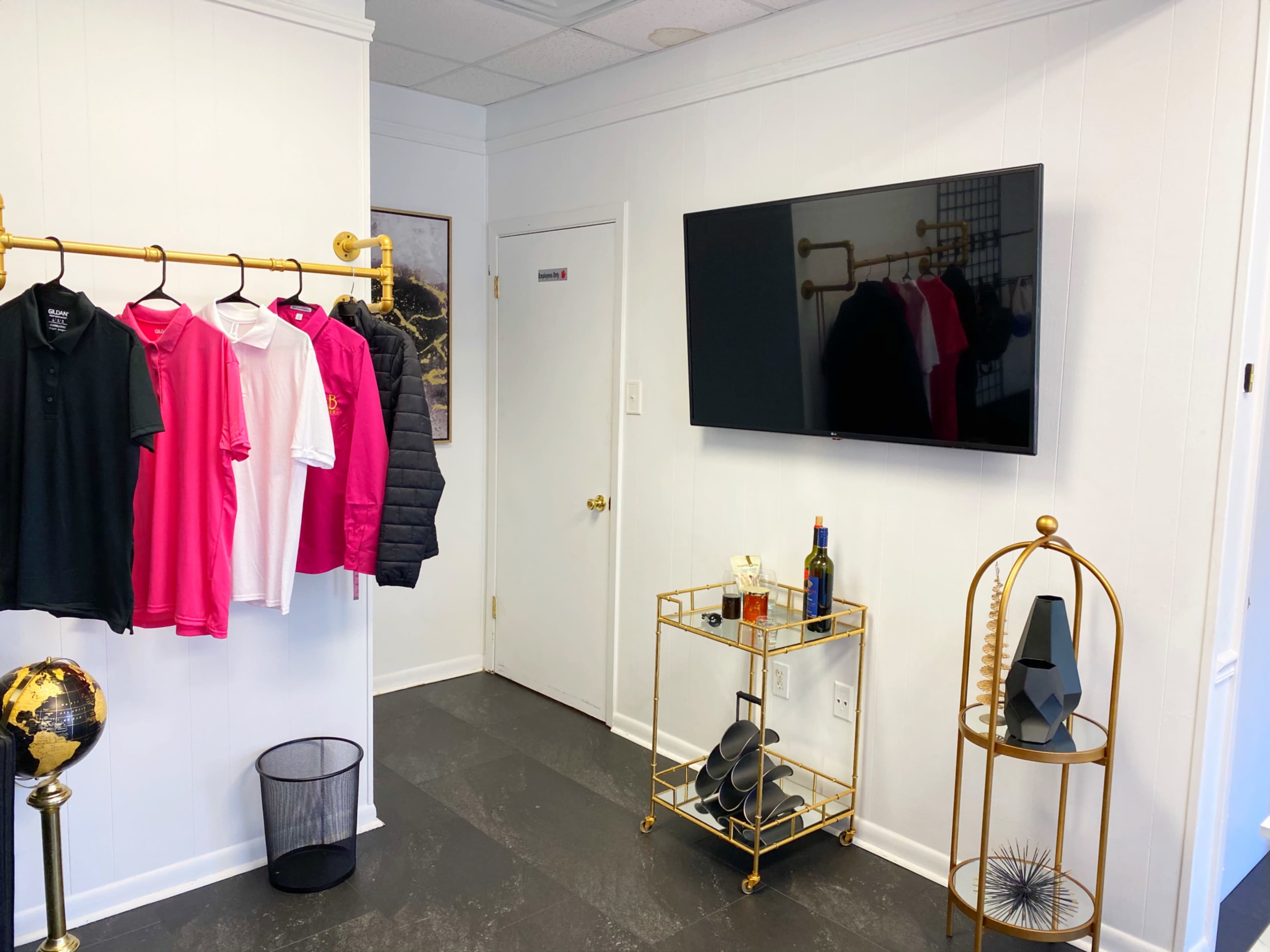 A neatly arranged room featuring a clothing rack with shirts, a wall-mounted television, a decorative cart with a bottle, and a globe stand.