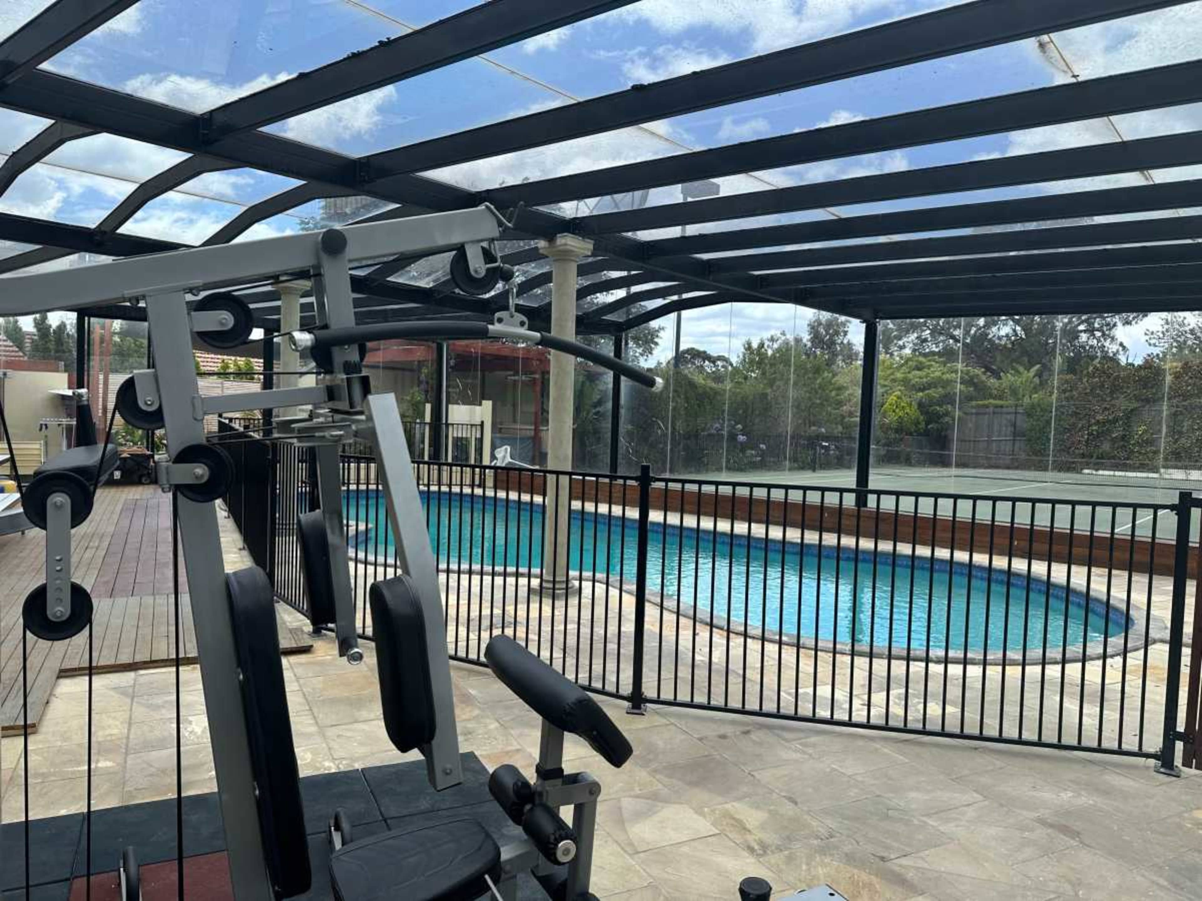 The image shows an indoor gym area featuring exercise equipment next to a swimming pool enclosed by a glass barrier.