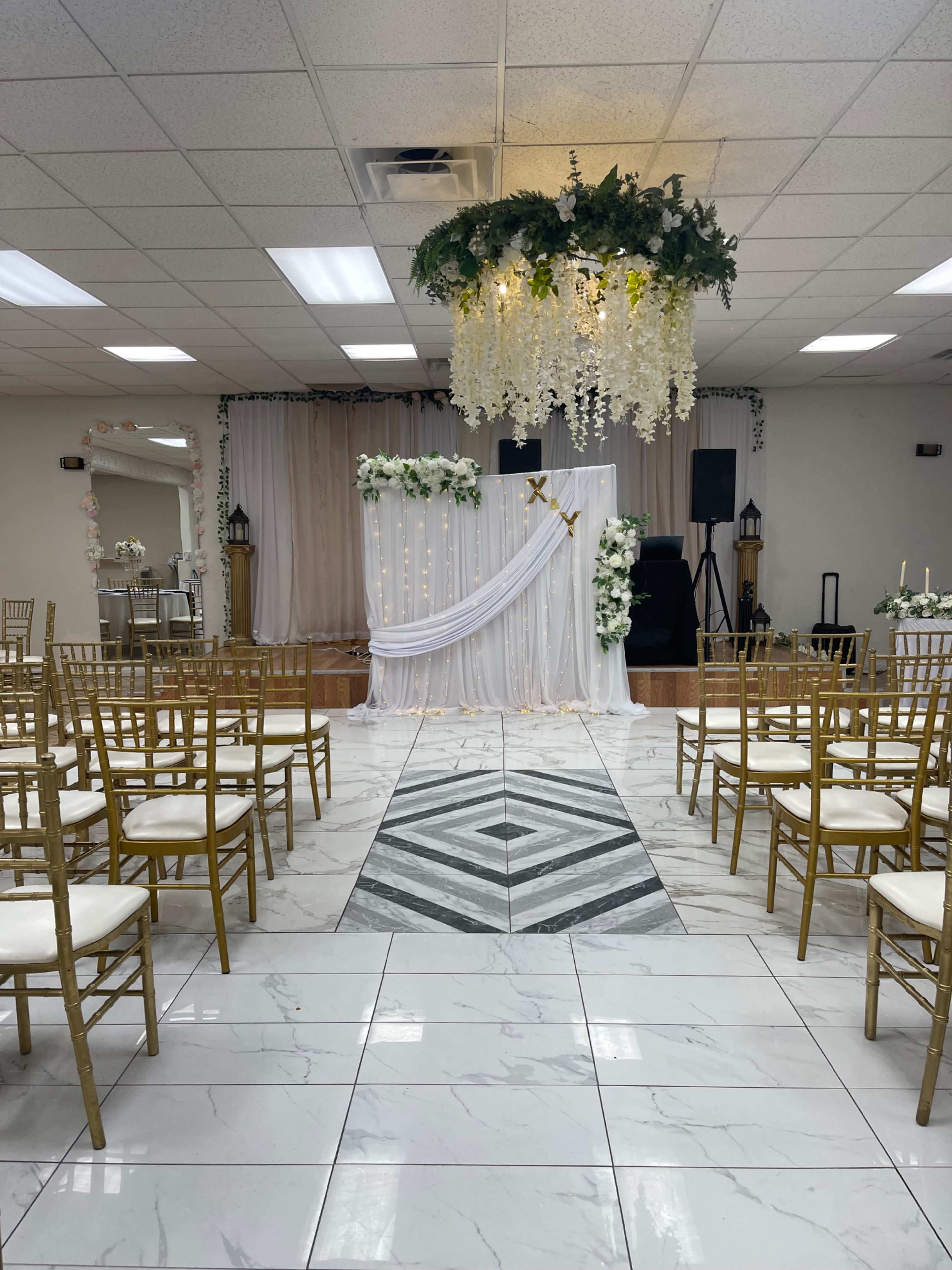 The image shows a wedding ceremony setup with rows of gold chairs facing a decorated altar featuring draped fabric and floral arrangements.