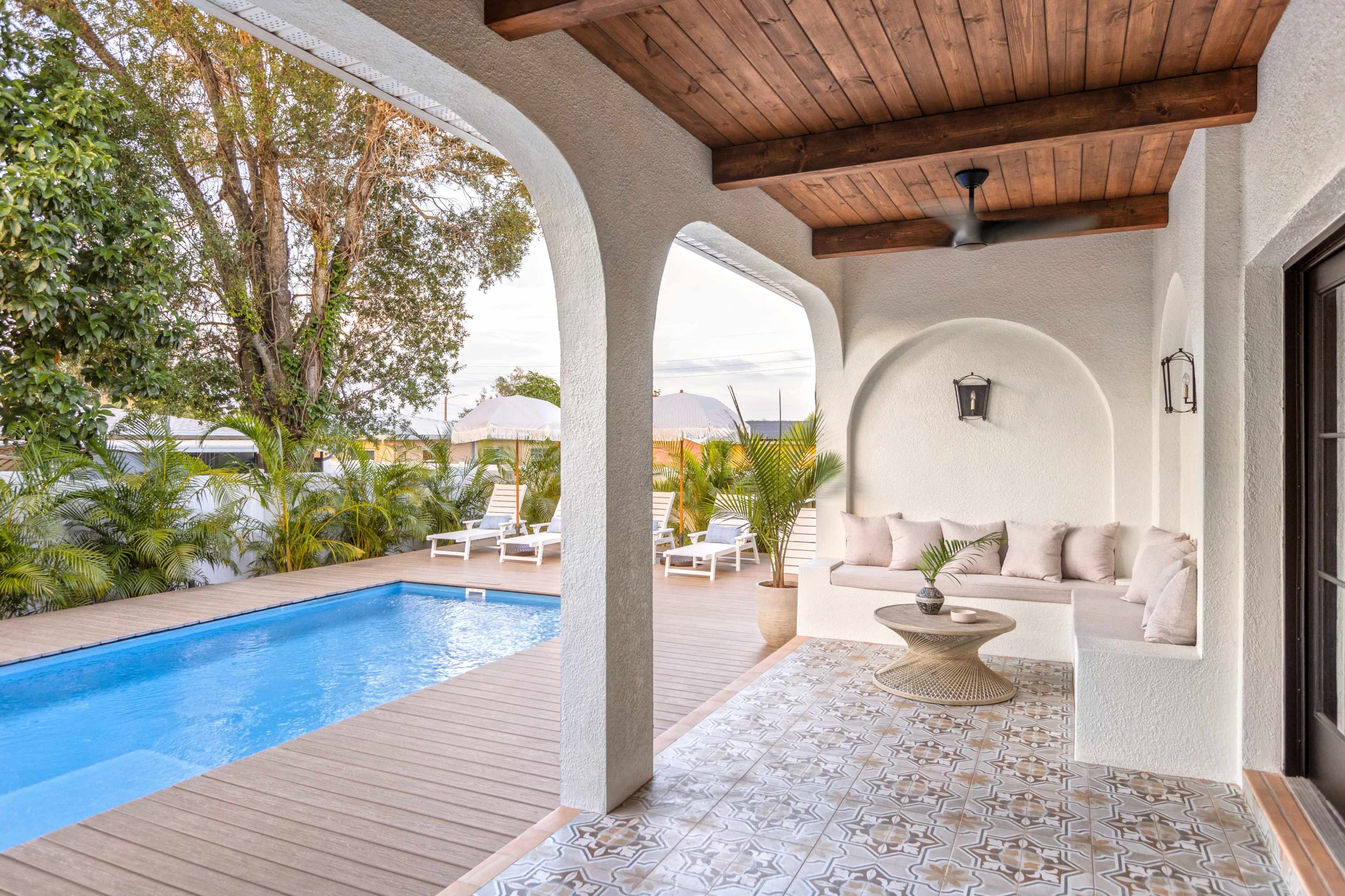 A patio area featuring a swimming pool, a wooden deck, and a seating arrangement under an overhanging porch.
