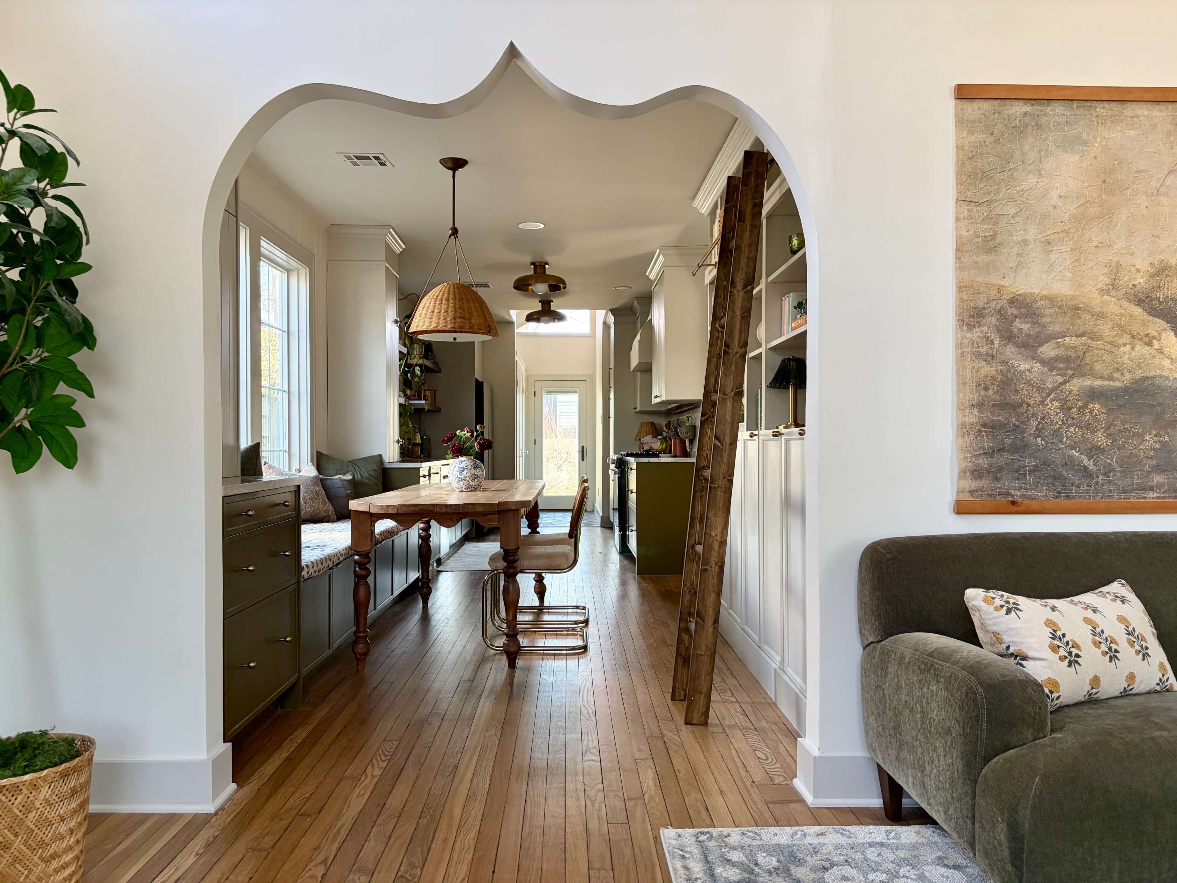 The image shows a cozy, well-lit interior featuring an arched doorway that leads from a living area to a dining space with a wooden table and chairs.