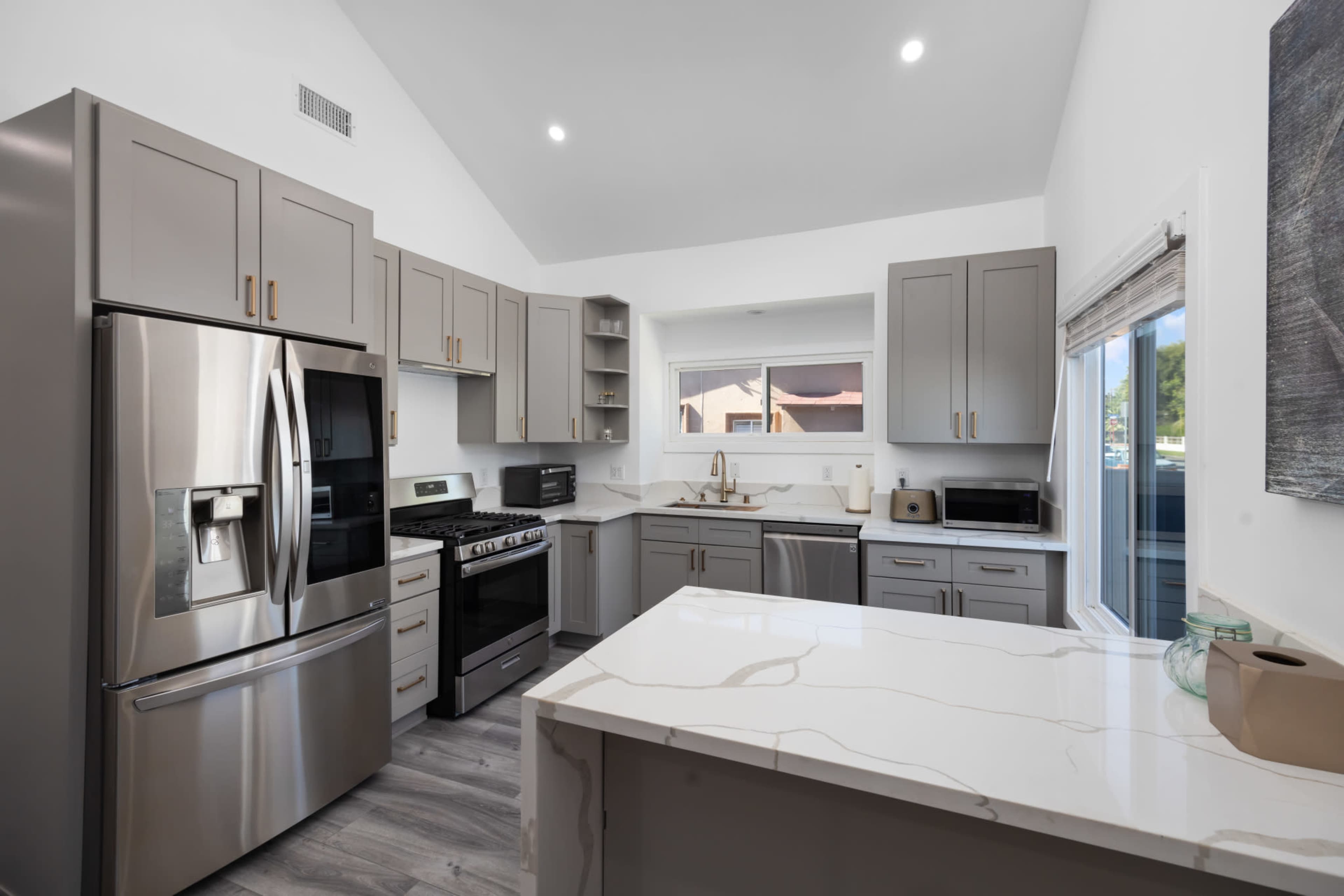 A modern kitchen features gray cabinetry, stainless steel appliances, and a white marble countertop.