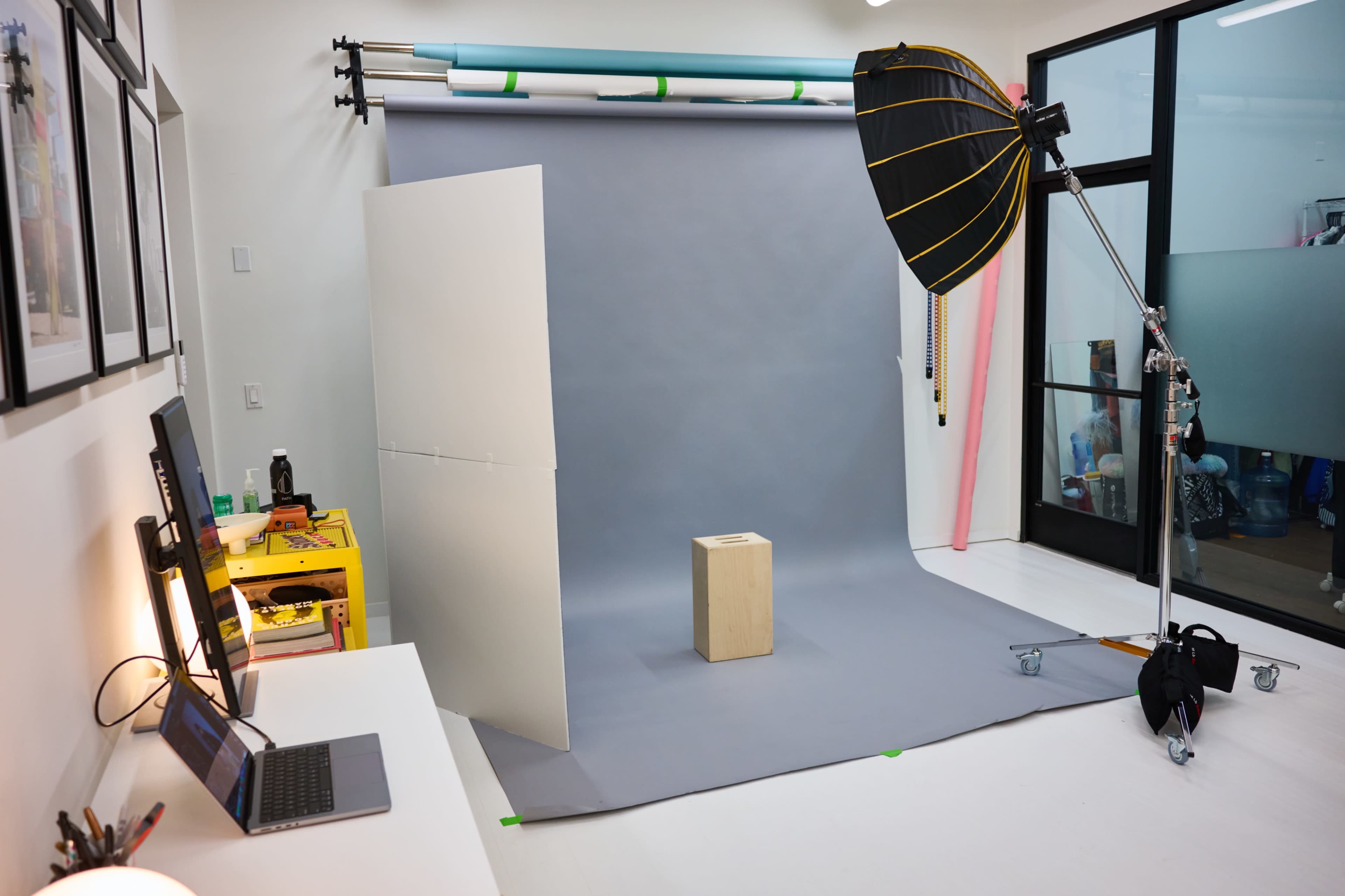 A photography studio setup with a gray backdrop, a light umbrella, and a wooden cube on the floor.