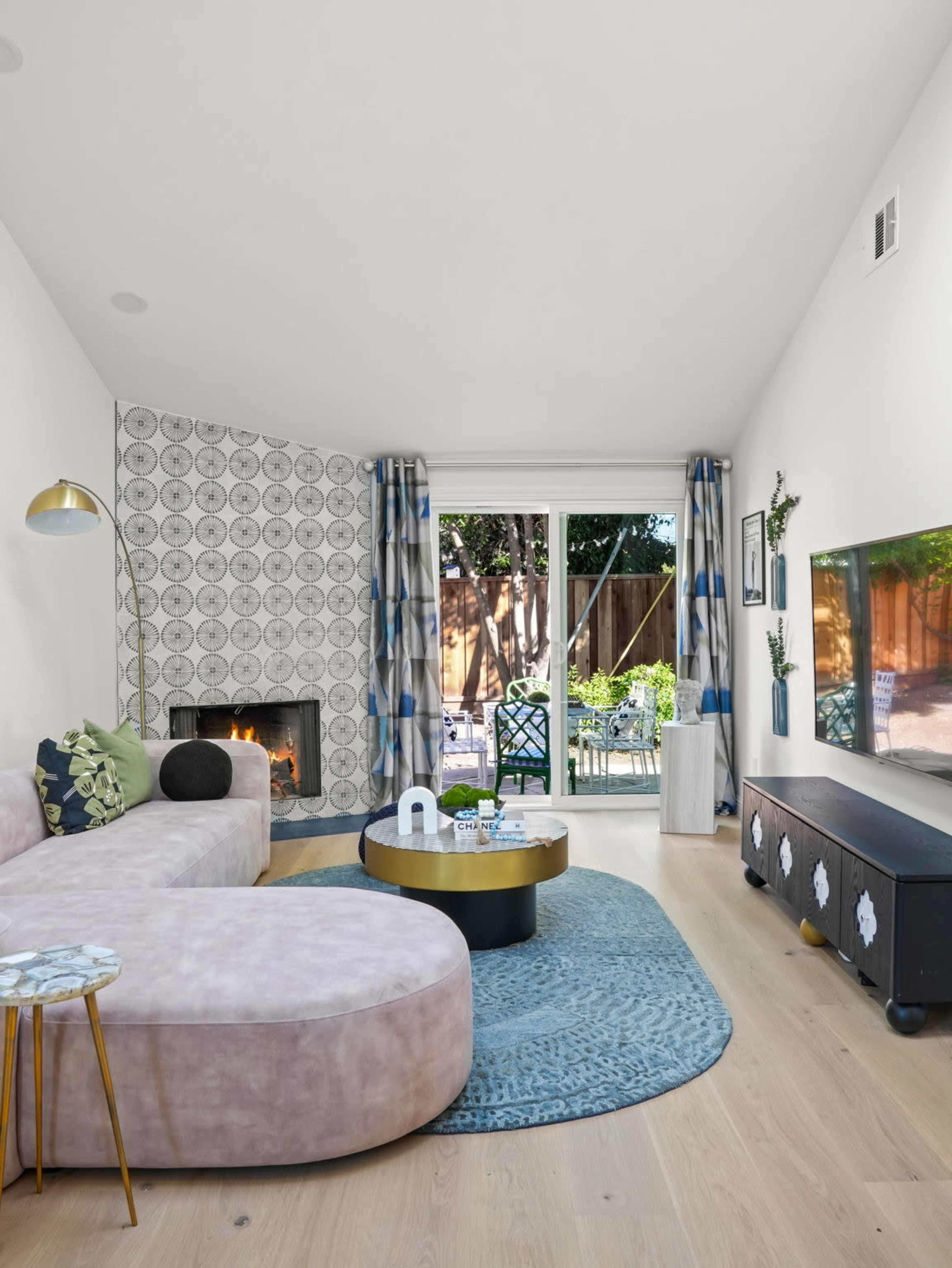 The living room features a curved pink sofa, a modern coffee table, and a large window with a view of the backyard garden.