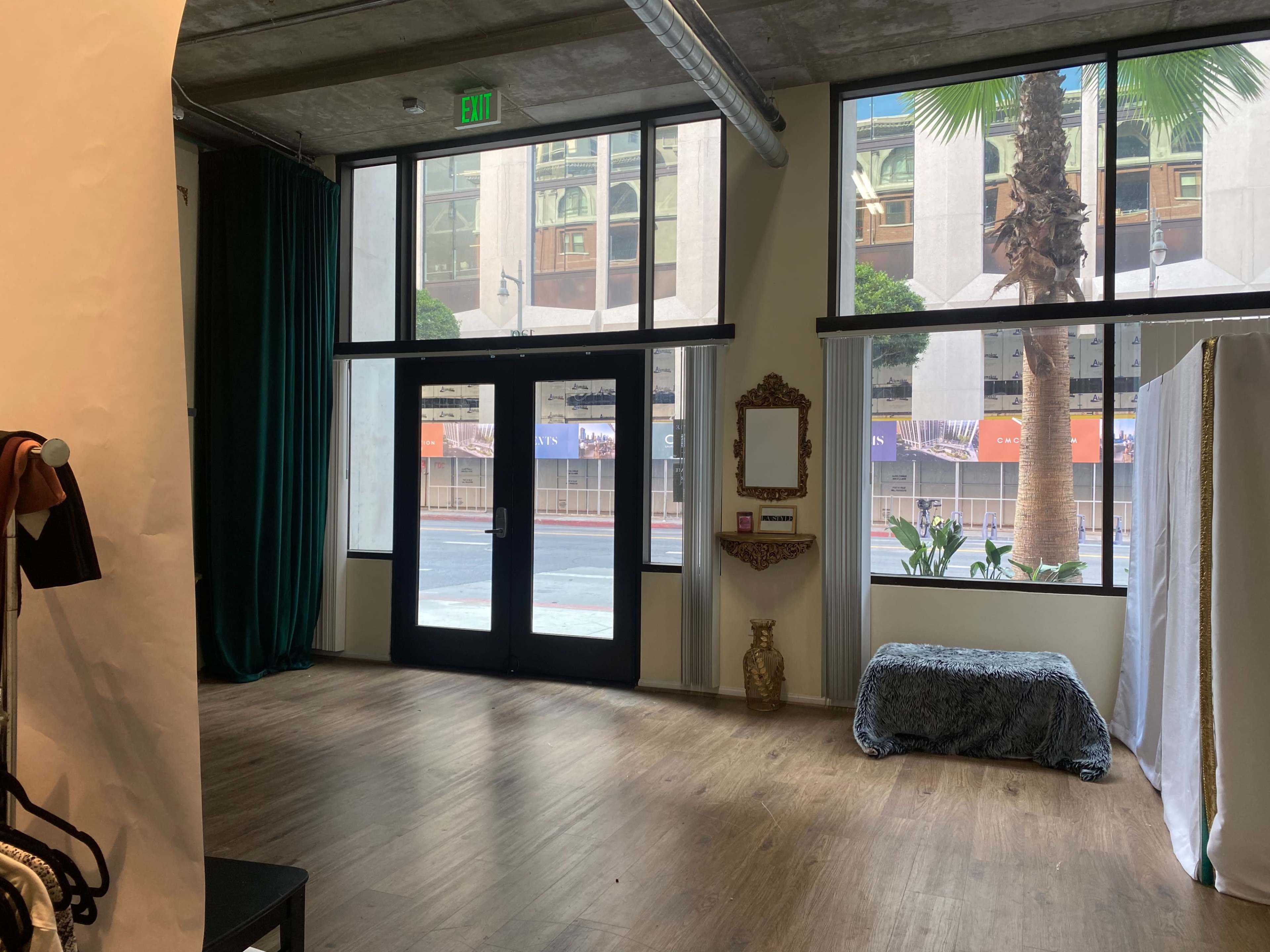 The scene shows an interior space with large windows, a bench covered with a blue cloth, a decorative mirror on the wall, and palm trees visible outside.