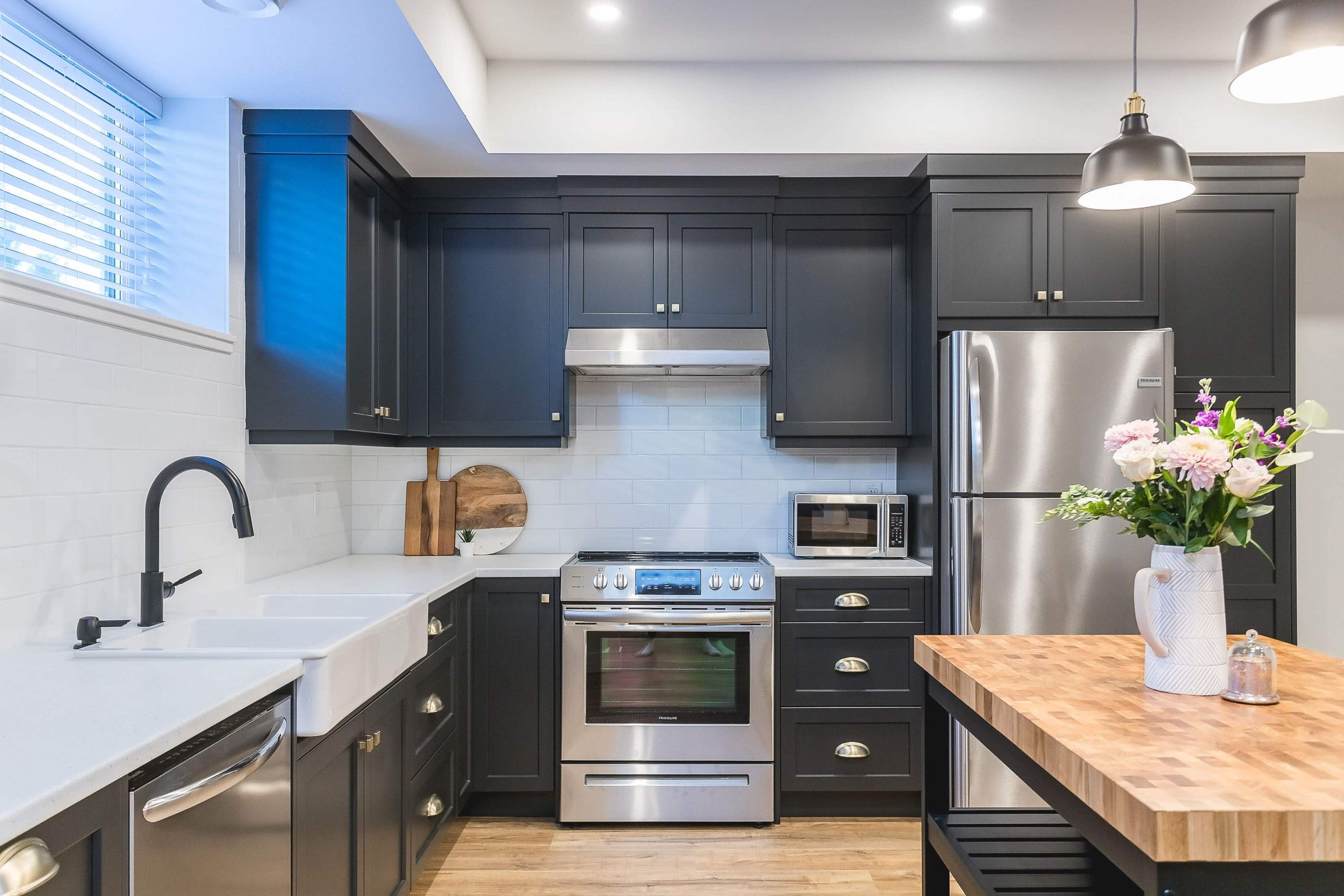 A modern kitchen featuring dark cabinetry, stainless steel appliances, and a wooden island with a flower arrangement.
