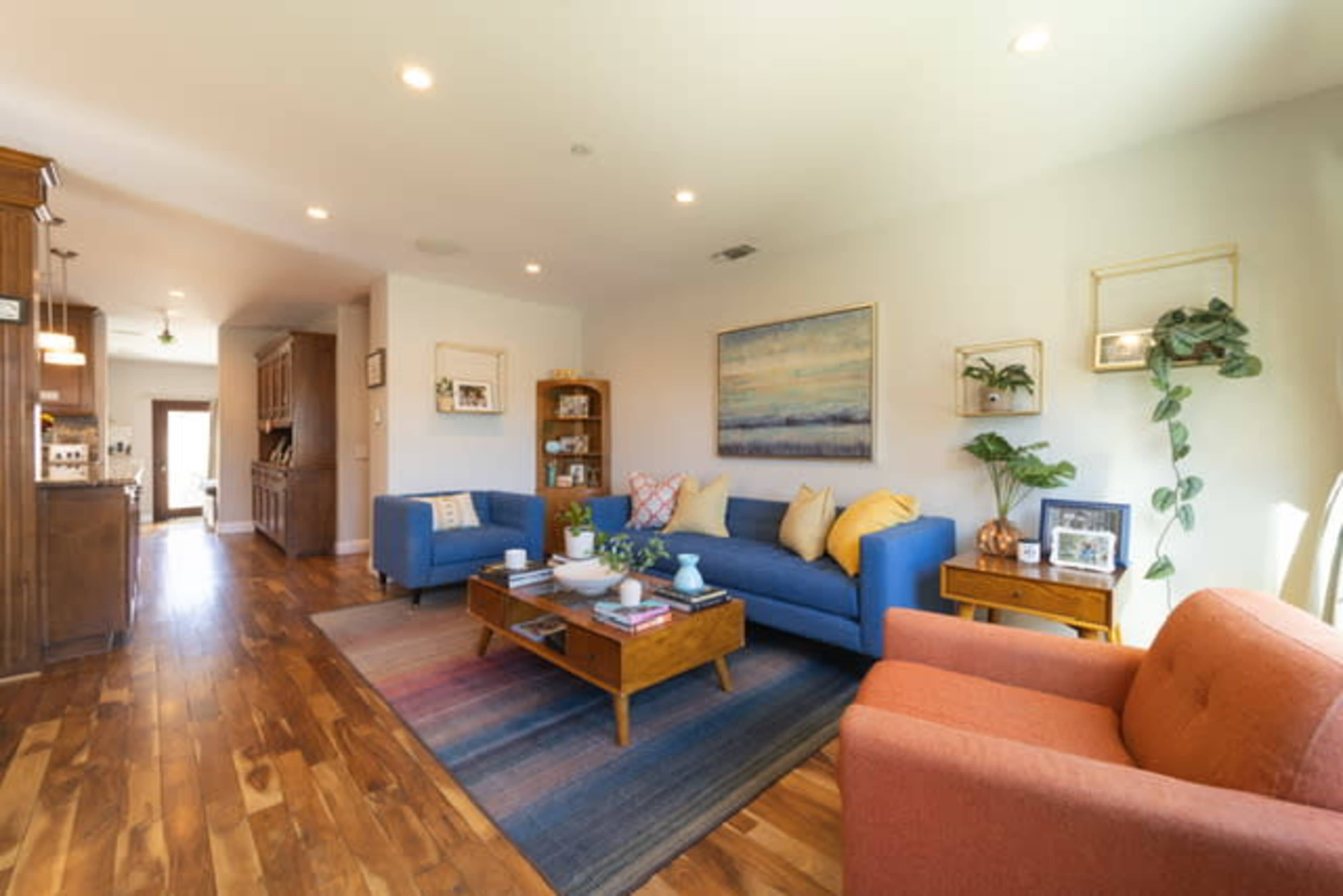 A modern living room featuring two blue sofas, an orange chair, a wooden coffee table, and various decorative items on the walls and furniture.