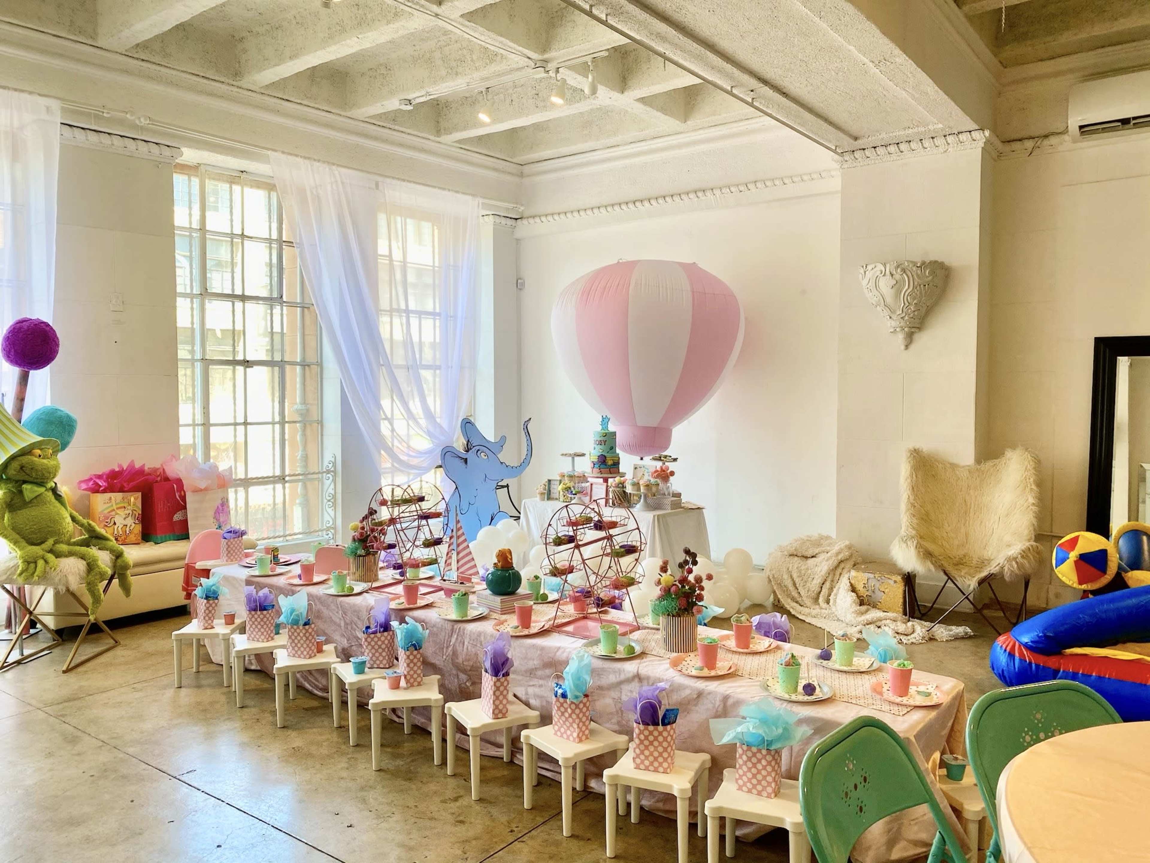A colorful children's party setup features a large table with treats, whimsical decorations, and seating arranged in a well-lit room.