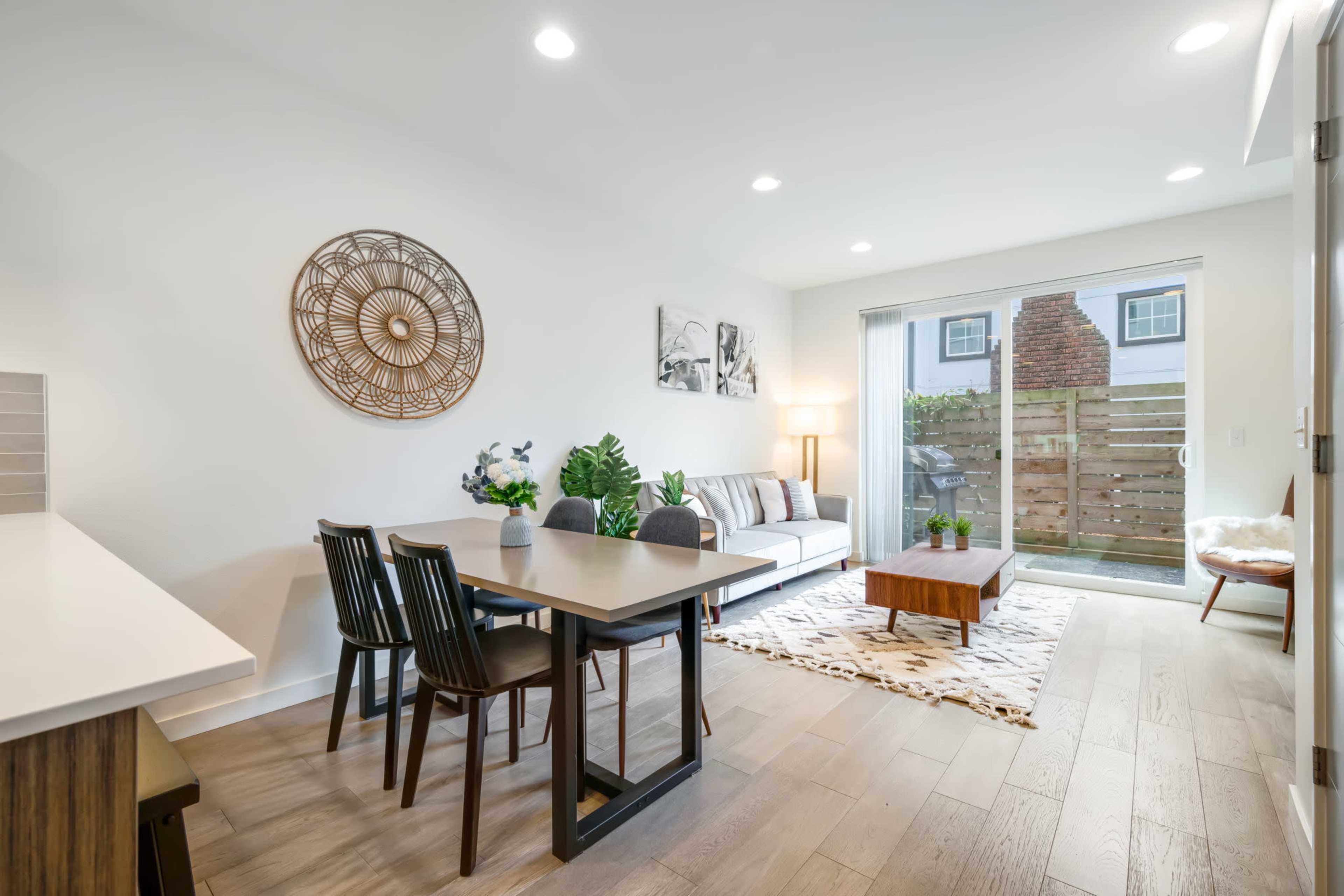 A modern living space features a dining area with a table and chairs, a cozy seating area with a sofa, and sliding glass doors leading to a small outdoor patio.