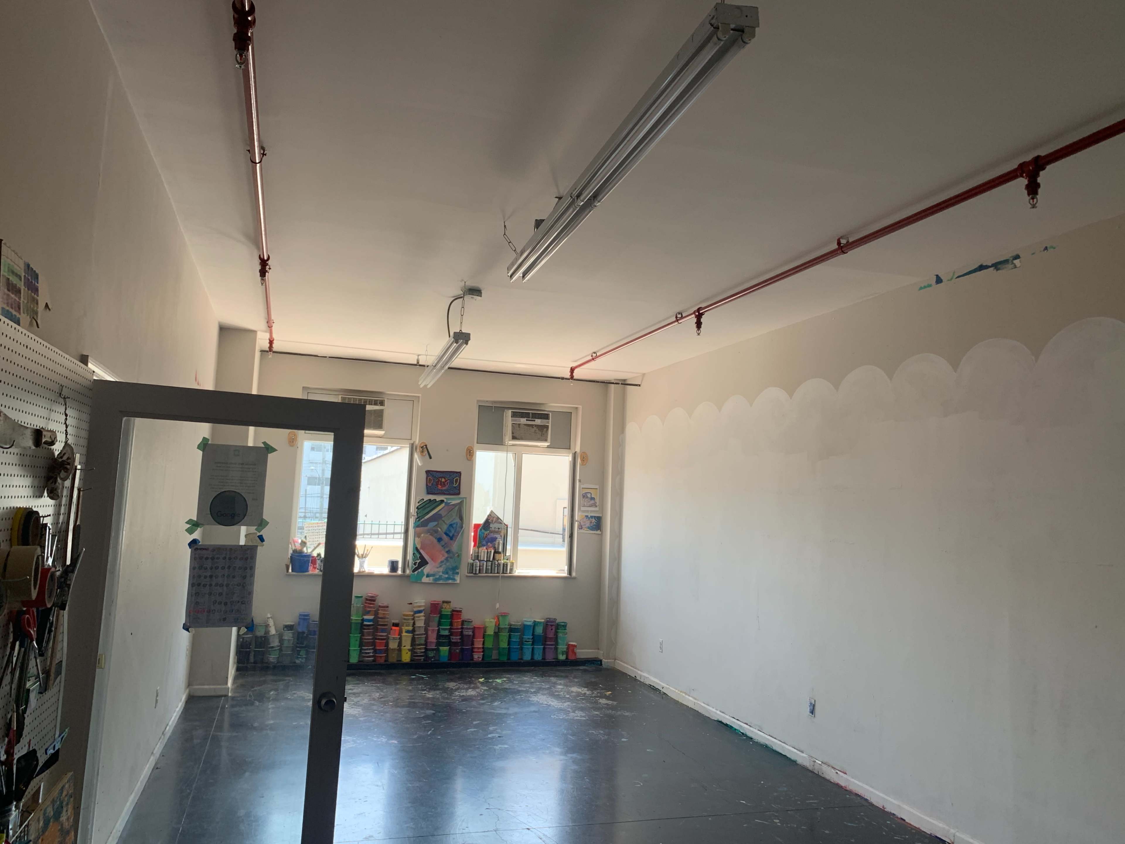 An empty room with two windows, overhead lighting, and colorful stacks of containers along one wall.