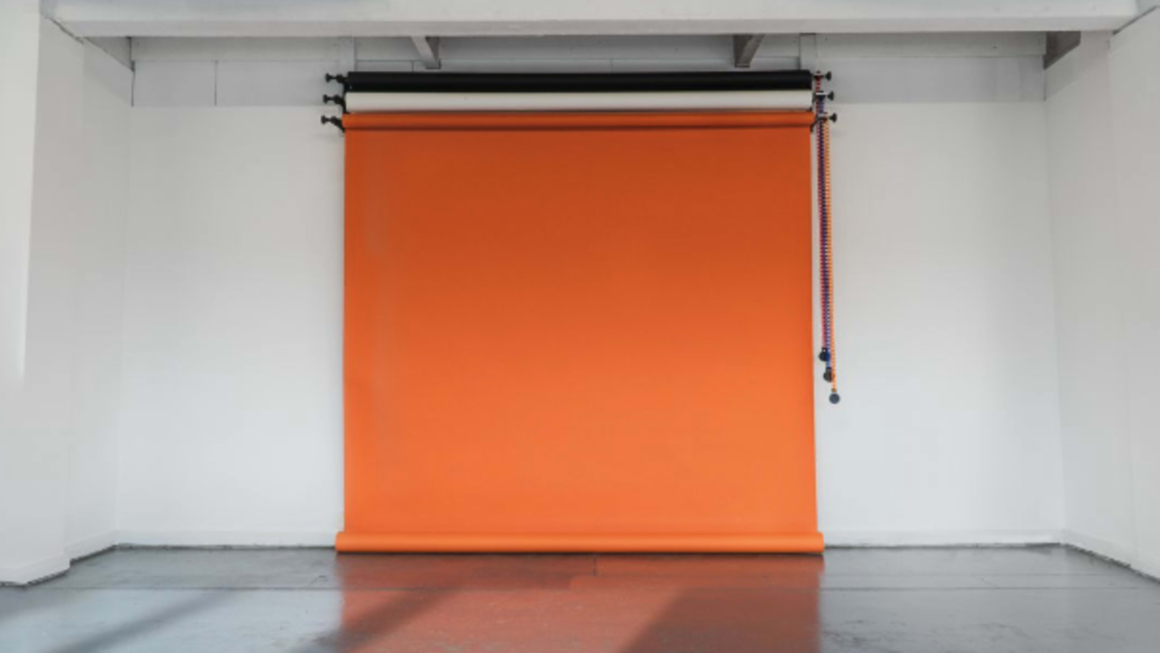 An empty room with a large orange backdrop roll hanging from a mounting system on the wall.