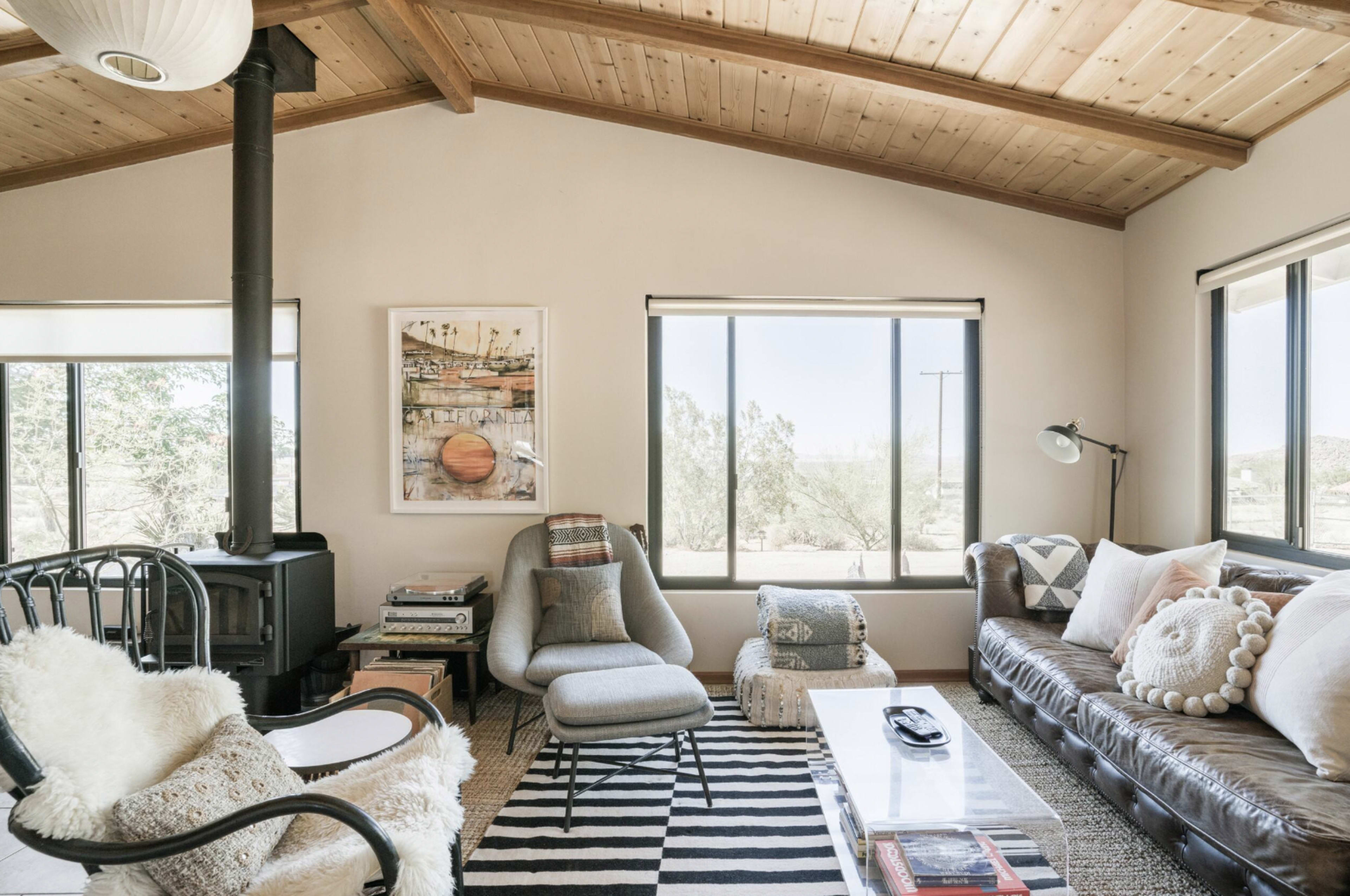 The living room features a leather sofa, a patterned rug, a modern armchair, and large windows showcasing a desert view.