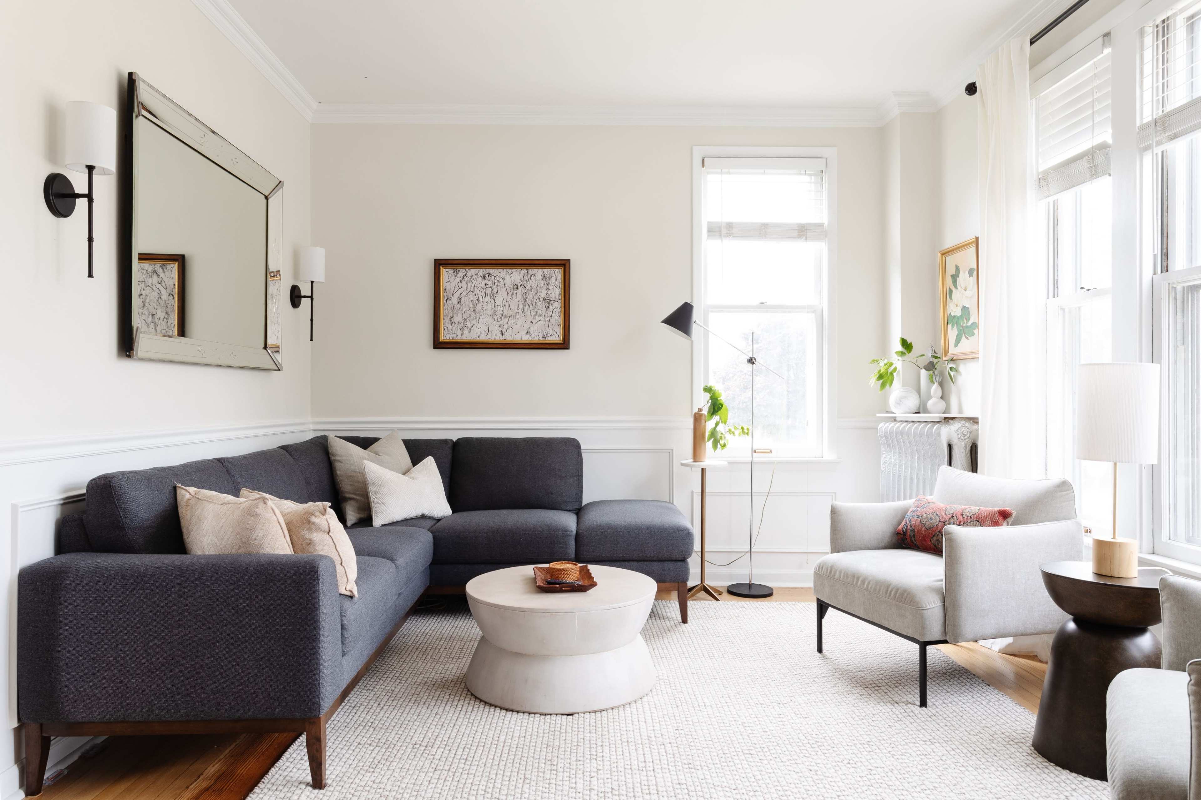 A modern living room with a gray sectional sofa, a round coffee table, and large windows allowing natural light to enter the space.