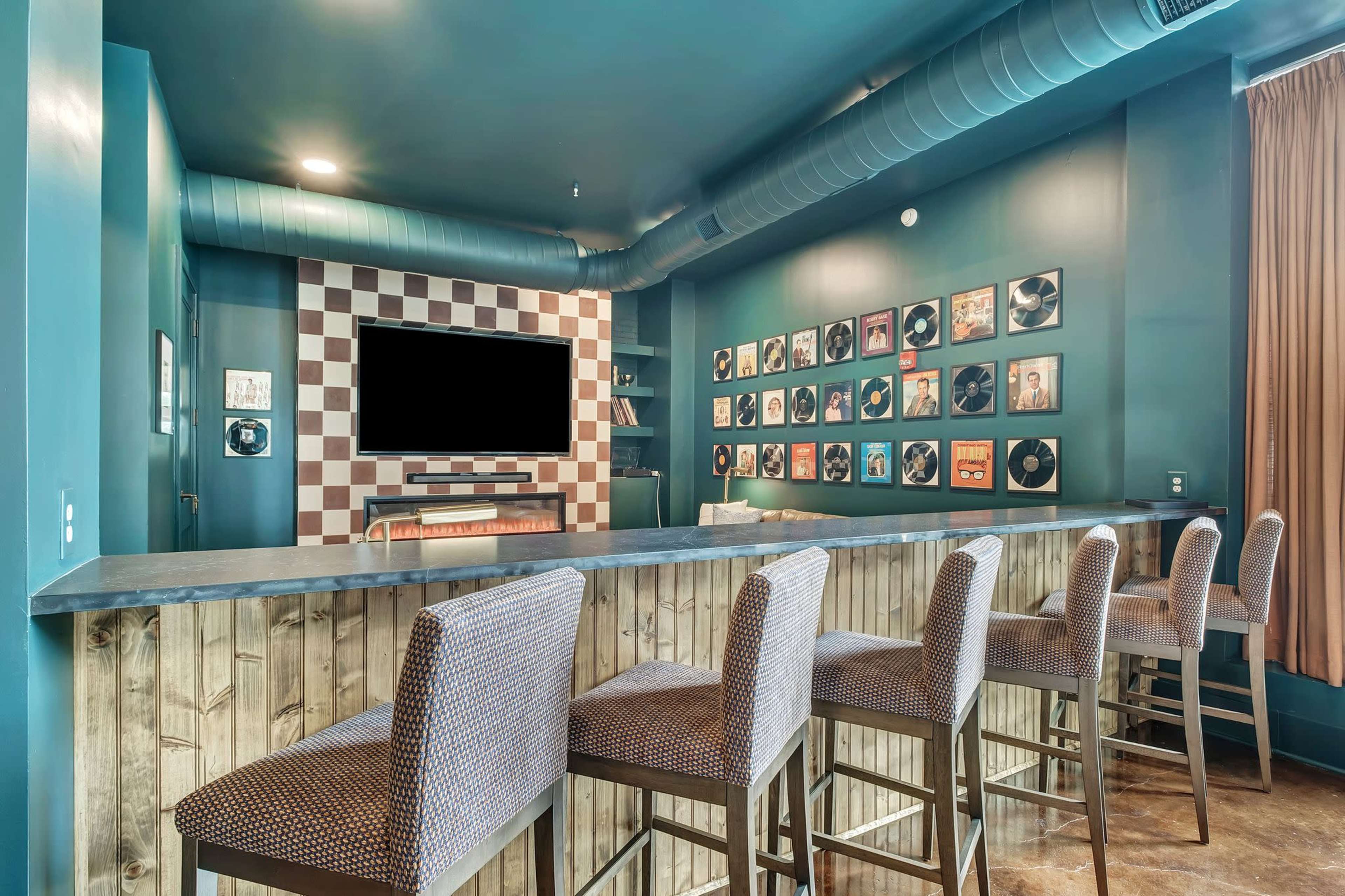 The image shows a modern bar area with a dark blue wall, a checkered accent wall, and several framed records displayed around a television.