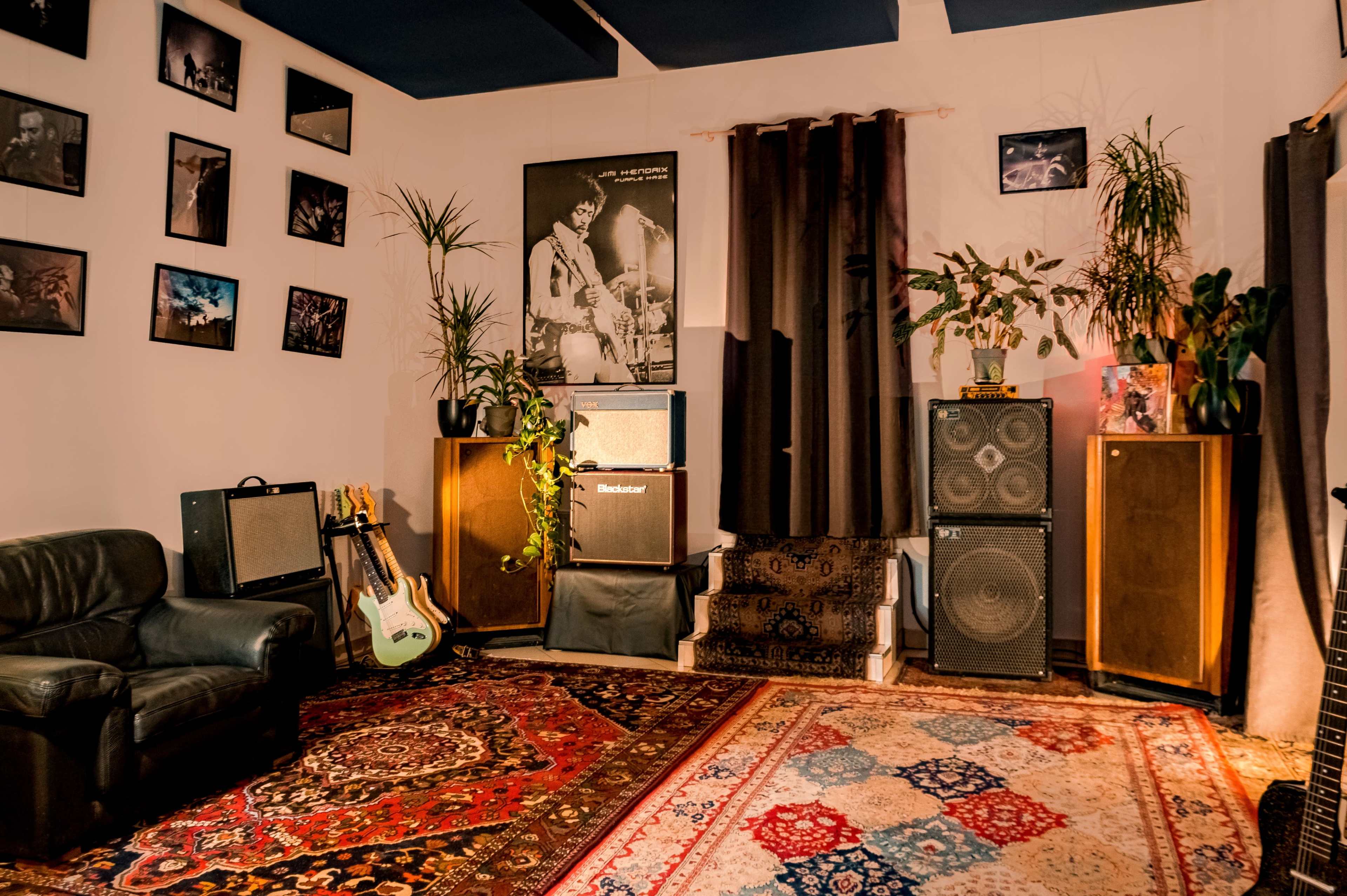 A cozy music room featuring a leather couch, an array of vintage amplifiers, plants, and framed photographs on the walls.