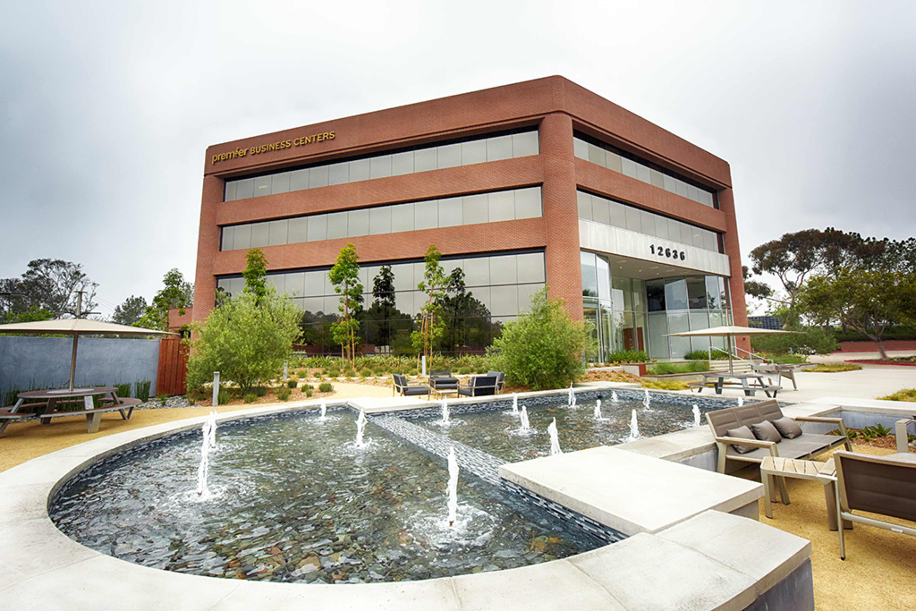 A modern, multi-story business center features a landscaped outdoor area with seating and a circular water feature.