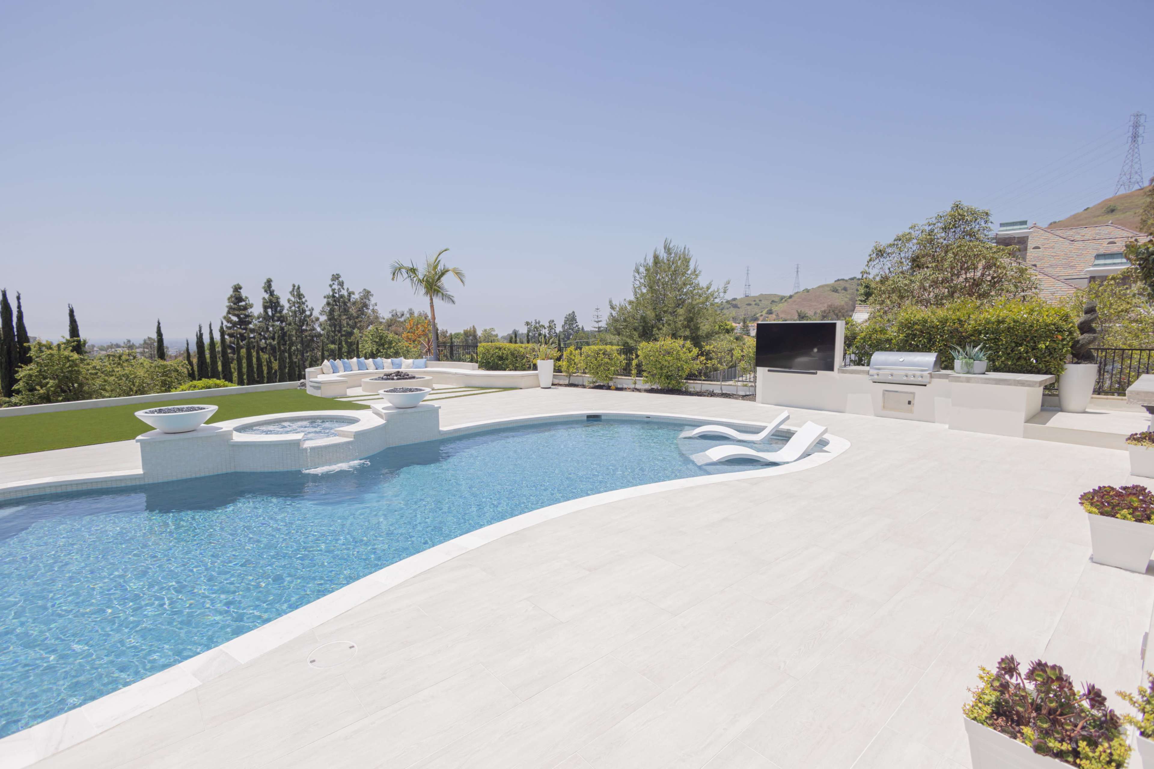 A modern swimming pool with a spa area, surrounded by landscaped greenery and outdoor amenities in a sunny setting.