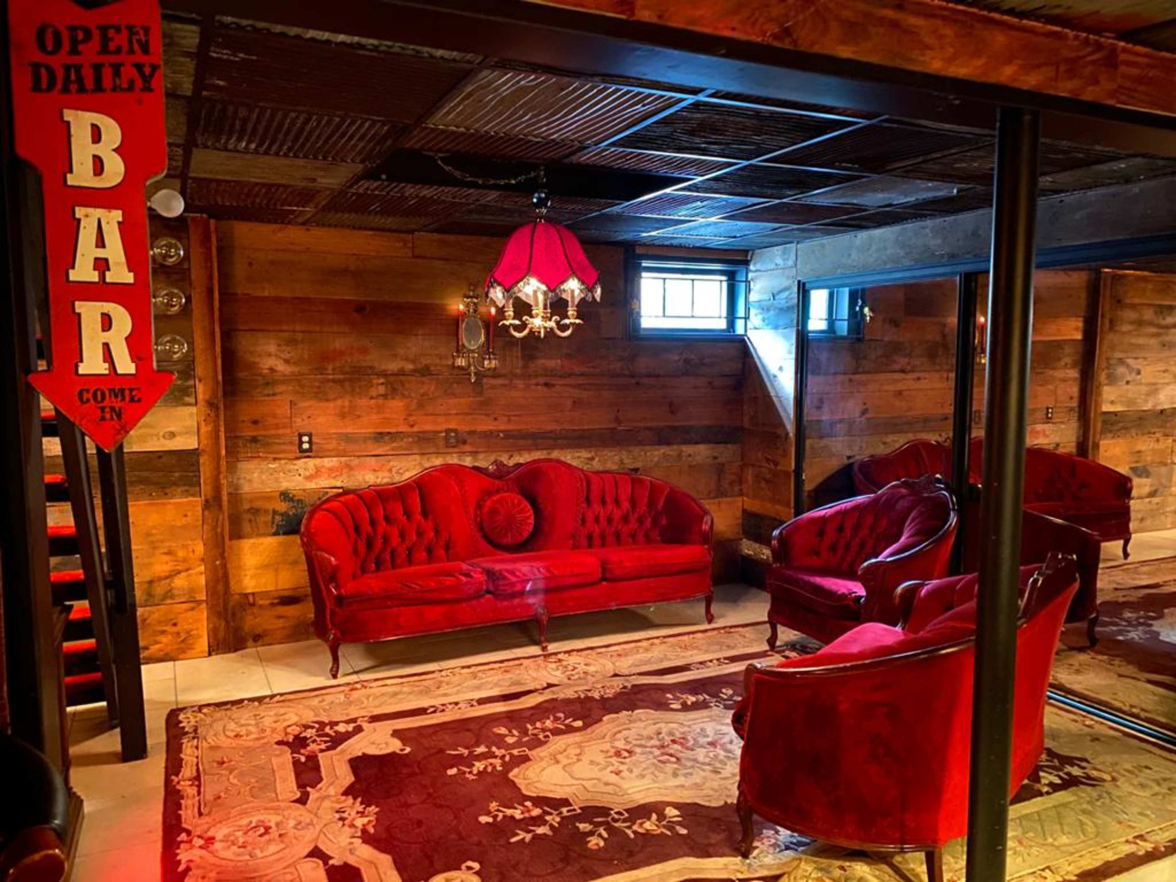 A bar area featuring red velvet seating, a chandelier, and wood-paneled walls.