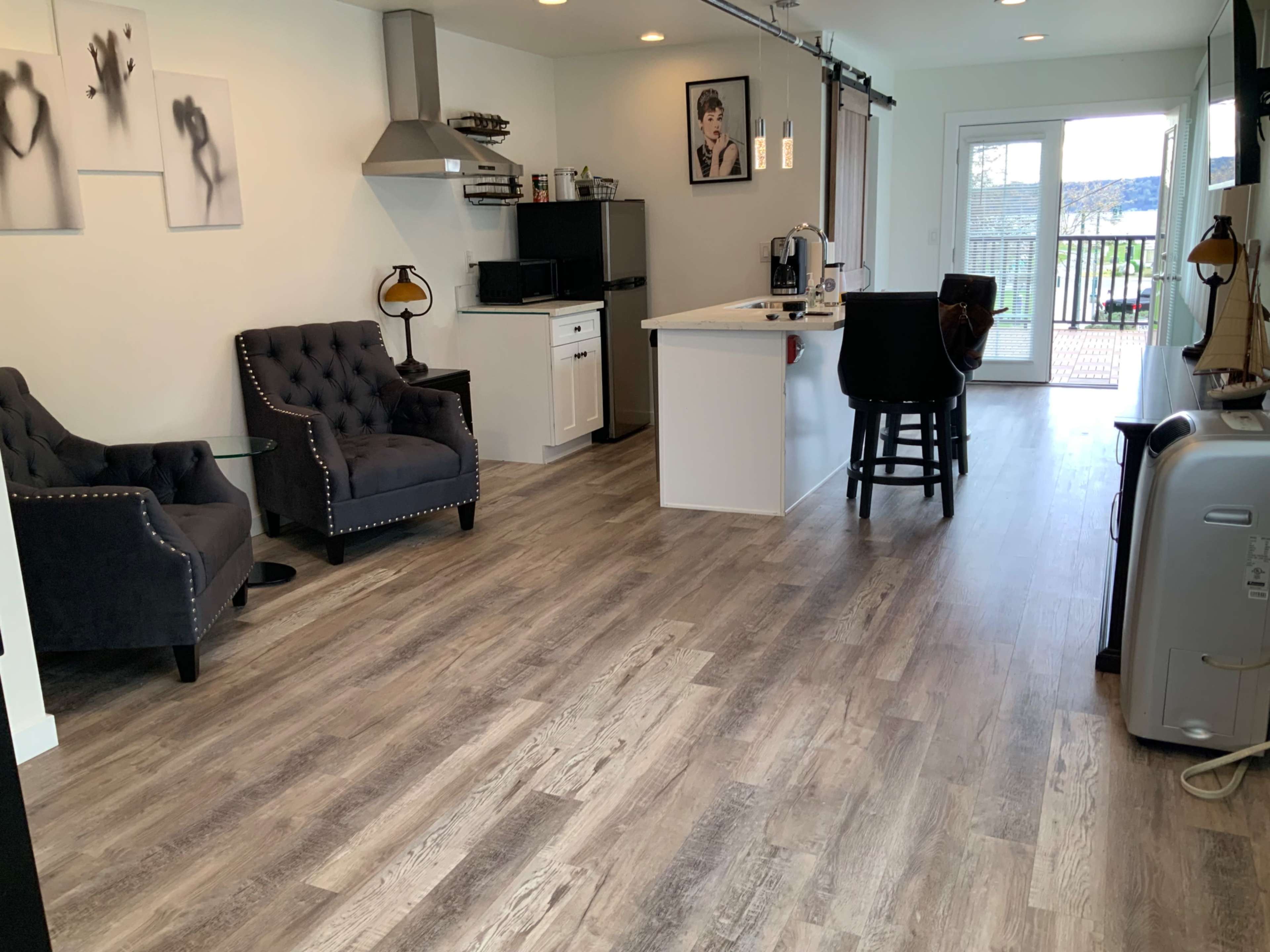 A modern living space with two armchairs, a kitchen area with appliances, and sliding glass doors leading to a deck.