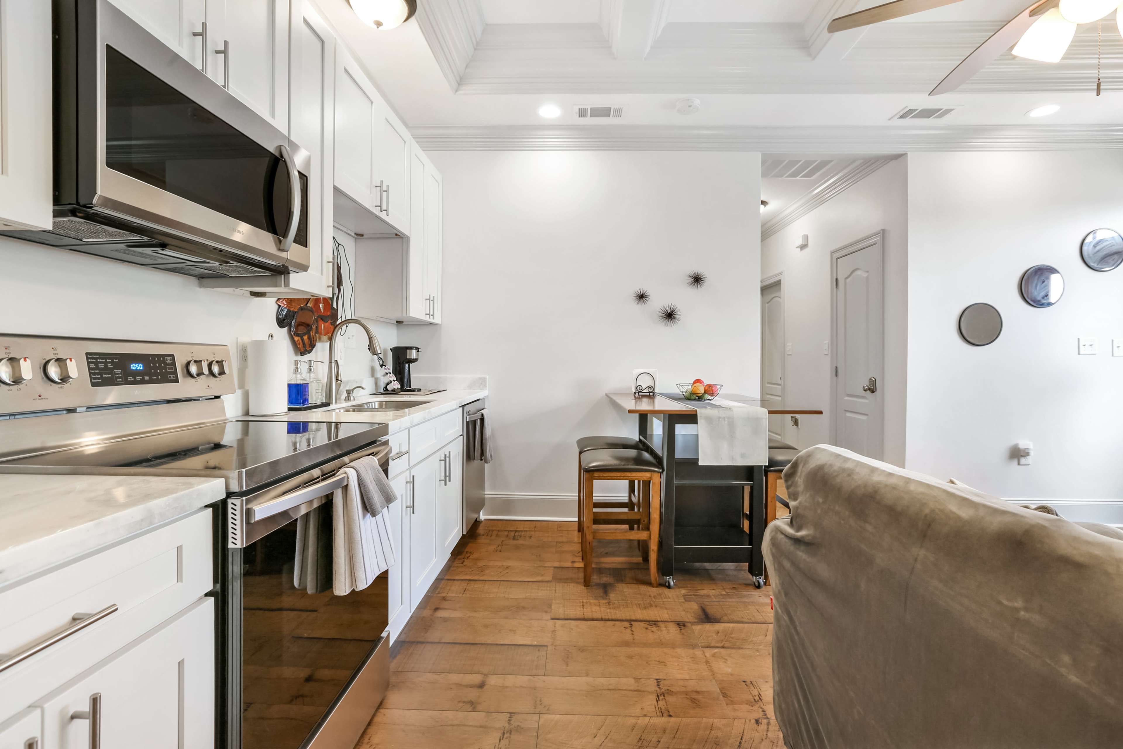 The image shows a modern kitchen with stainless steel appliances, white cabinetry, and a small dining area with two barstools.